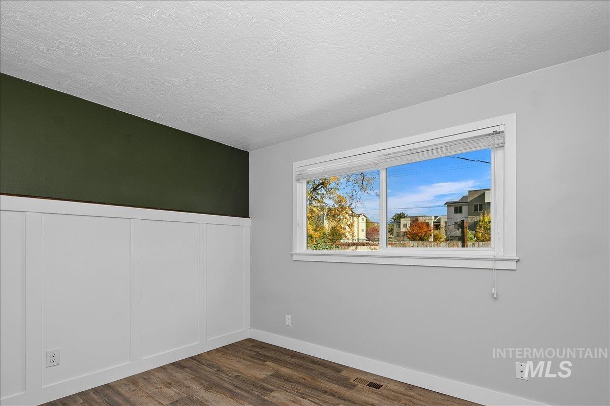 Empty room featuring dark wood-type flooring, a textured ceiling, and wainscoting