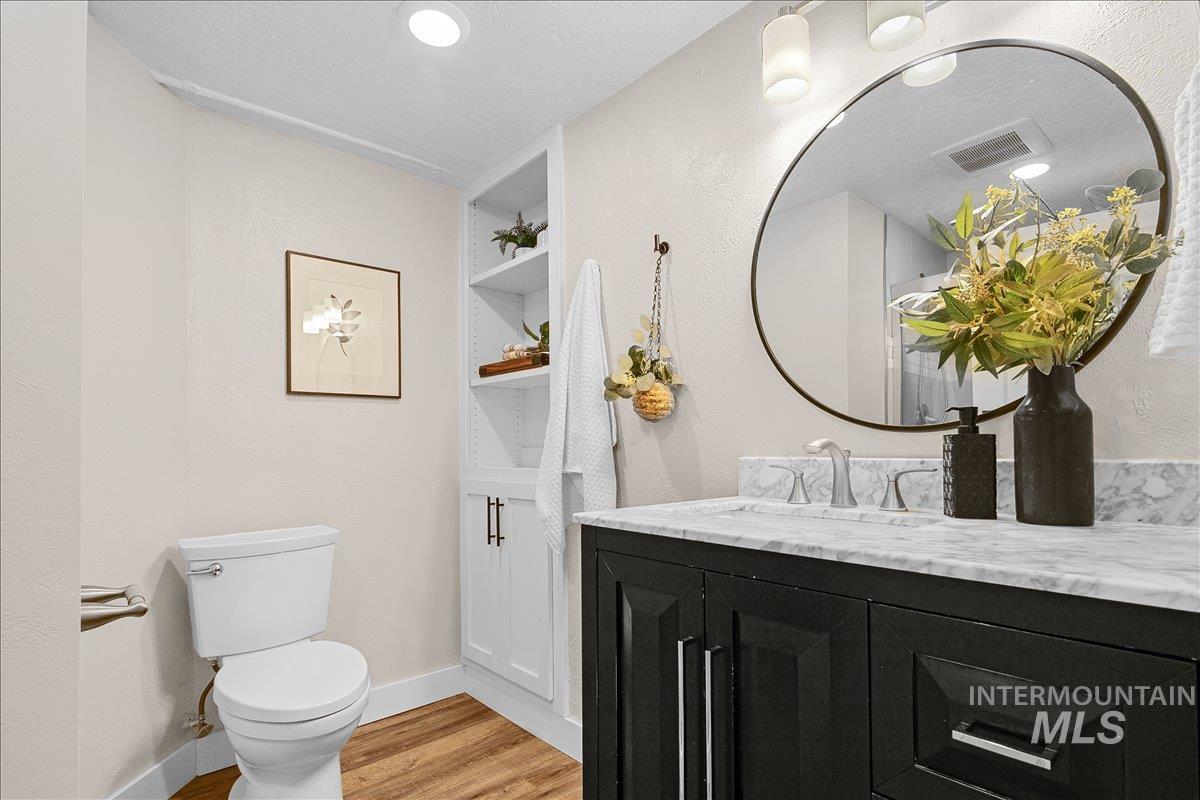 Half bath with vanity, light wood finished floors, a textured wall, and a textured ceiling