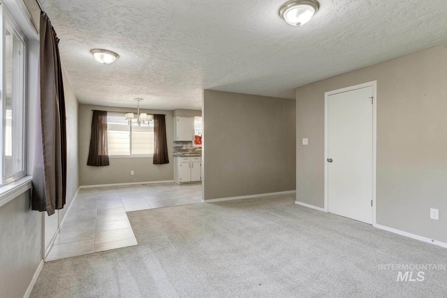 Empty room with light carpet, a textured ceiling, light tile patterned floors, and a chandelier