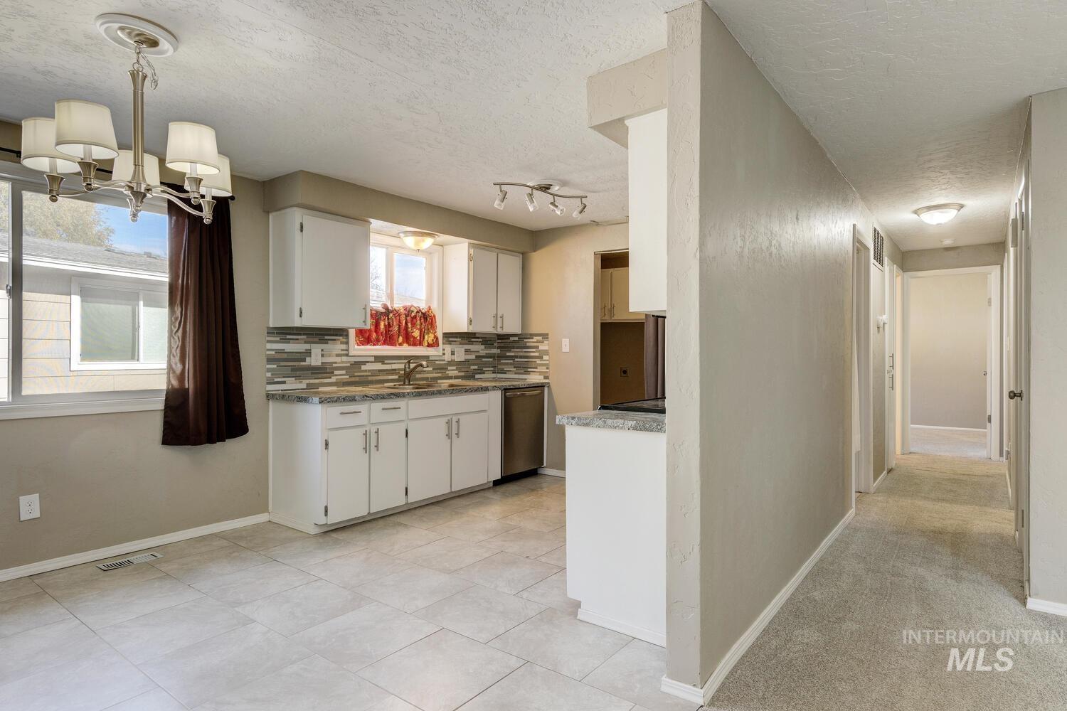 Kitchen featuring tasteful backsplash, a textured ceiling, white cabinets, stainless steel dishwasher, and light tile patterned flooring
