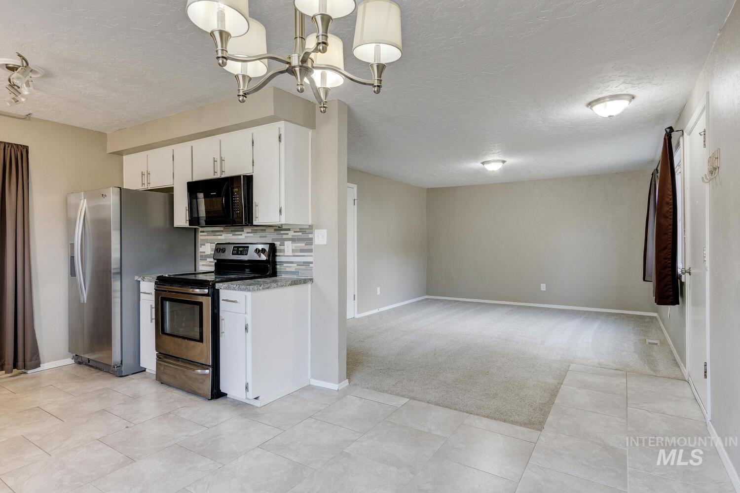 Kitchen featuring stainless steel electric stove, decorative backsplash, white cabinetry, black microwave, and light carpet