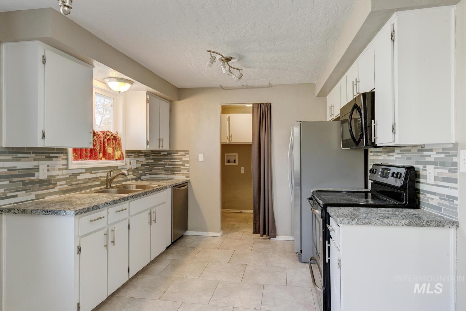Kitchen featuring backsplash, stainless steel appliances, white cabinetry, and a textured ceiling
