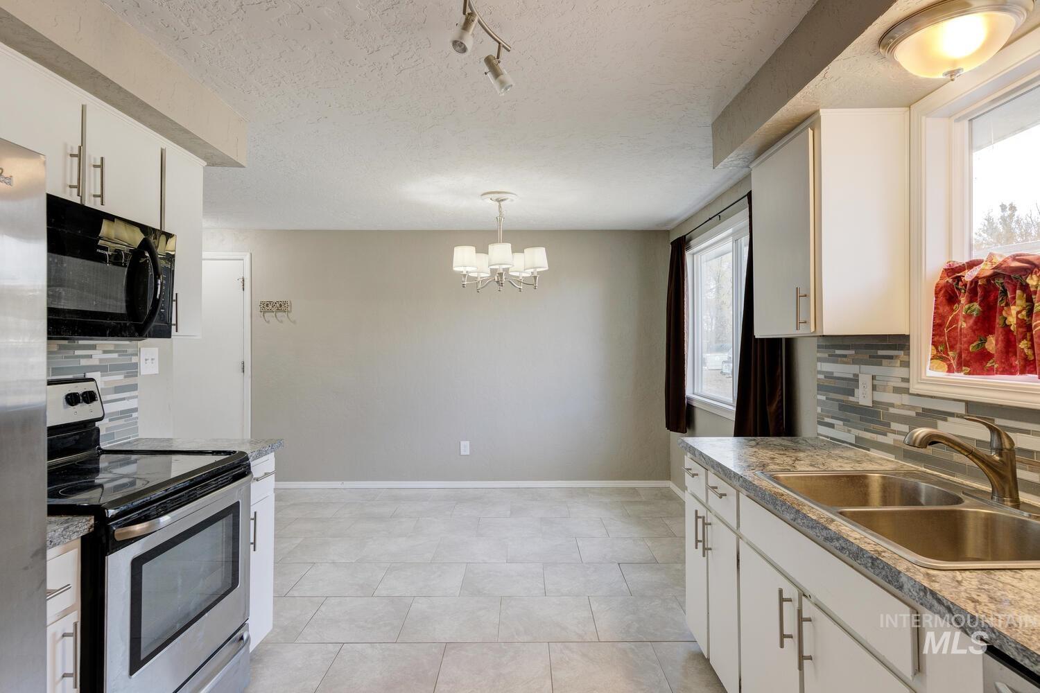 Kitchen featuring appliances with stainless steel finishes, tasteful backsplash, white cabinets, a textured ceiling, and a chandelier