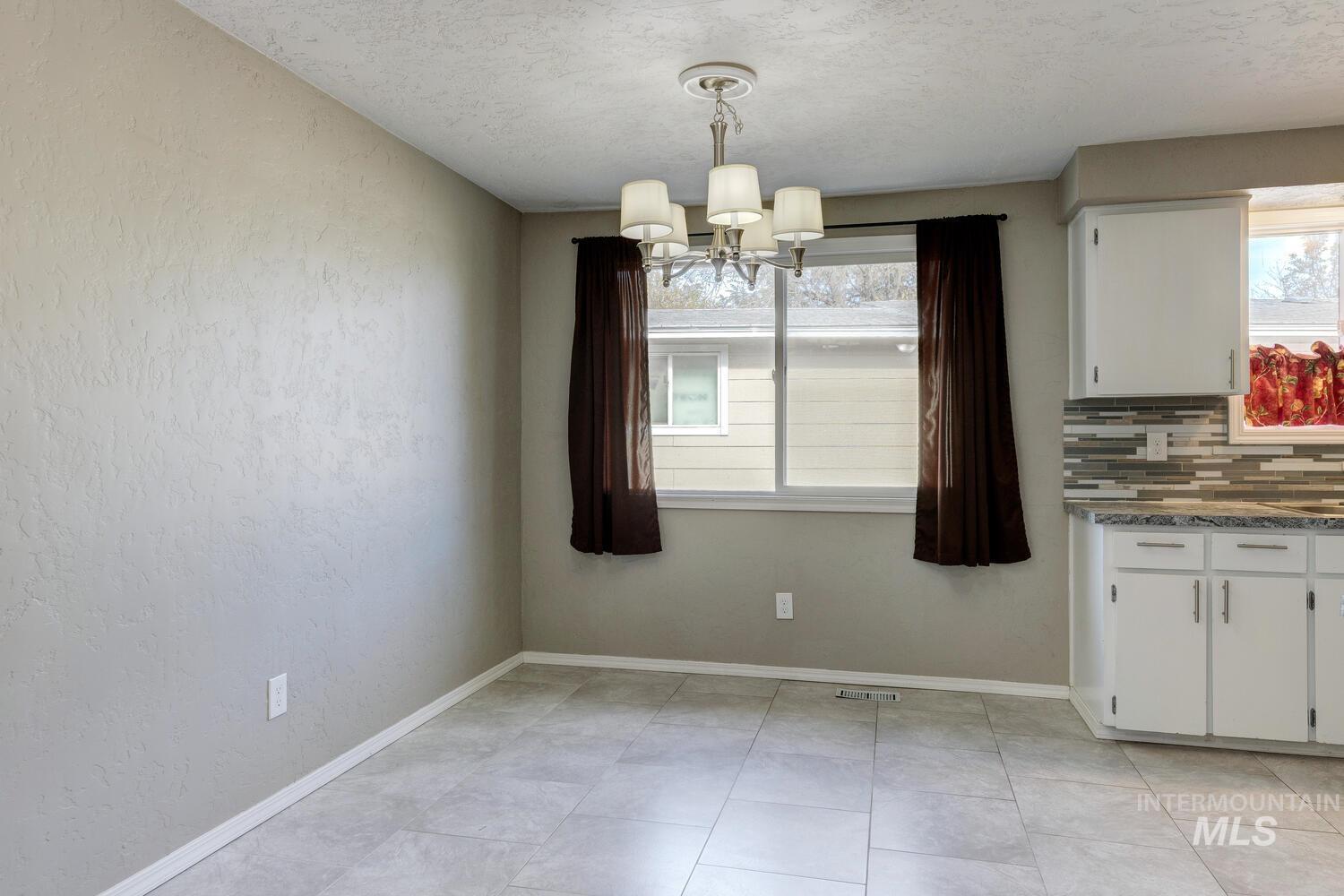 Unfurnished dining area with a textured wall, a textured ceiling, a chandelier, and light tile patterned floors