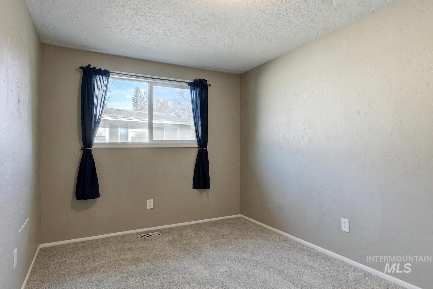 Carpeted spare room with a textured ceiling and a textured wall