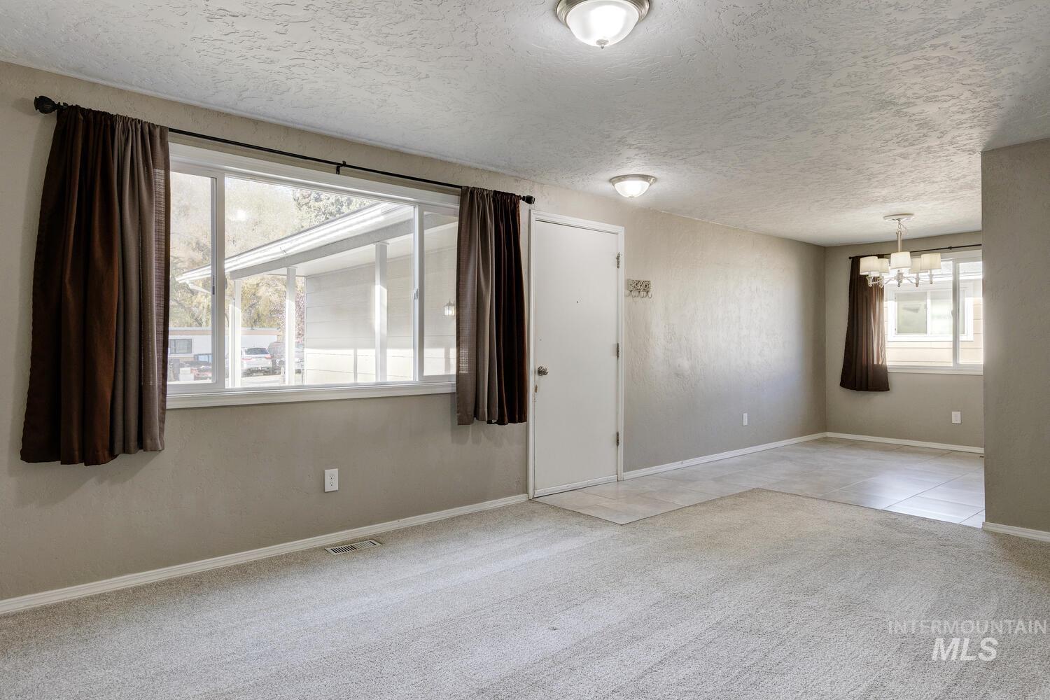 Empty room with light colored carpet, a textured ceiling, and a chandelier