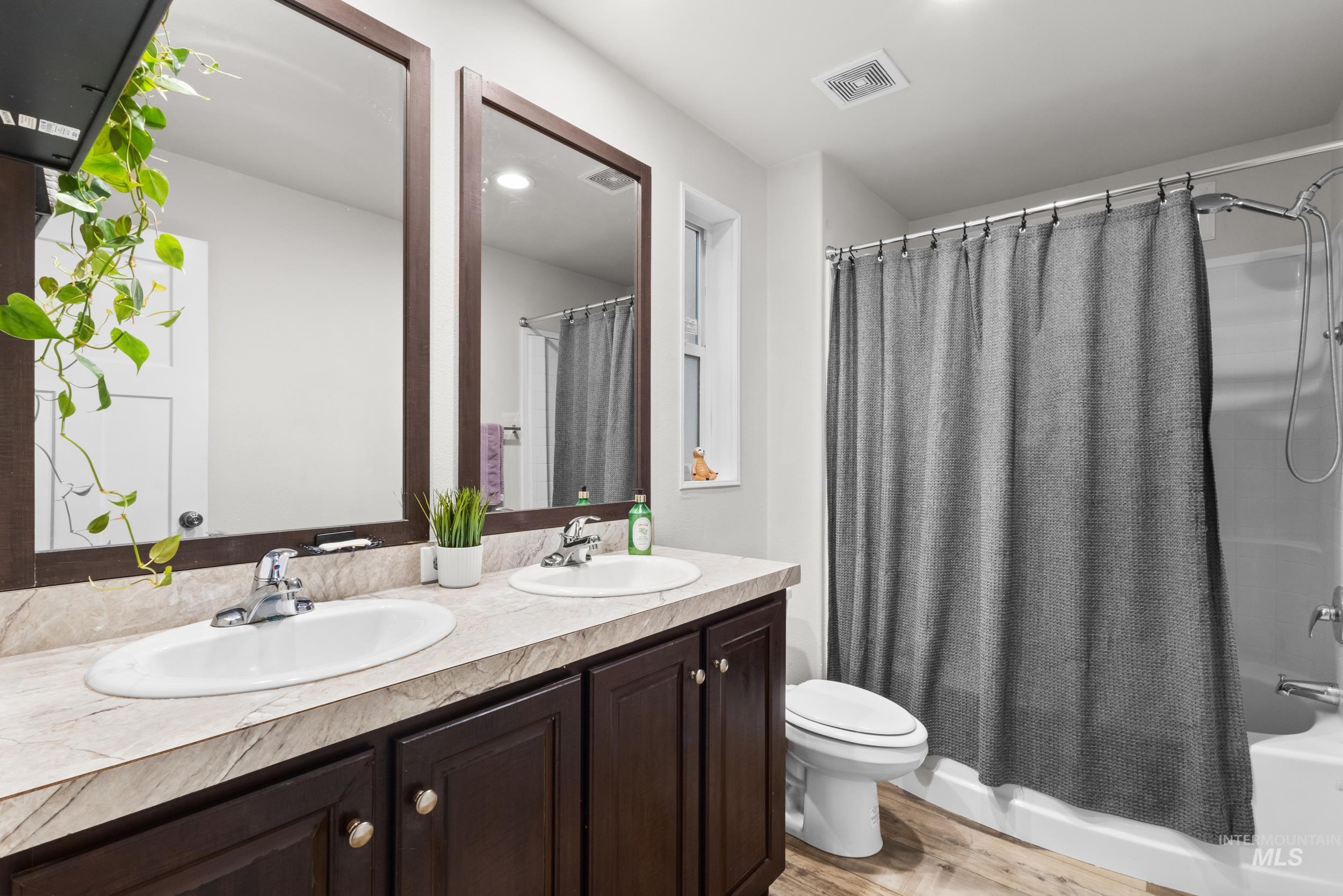 Bathroom featuring shower / bathtub combination with curtain, double vanity, light wood finished floors, and recessed lighting