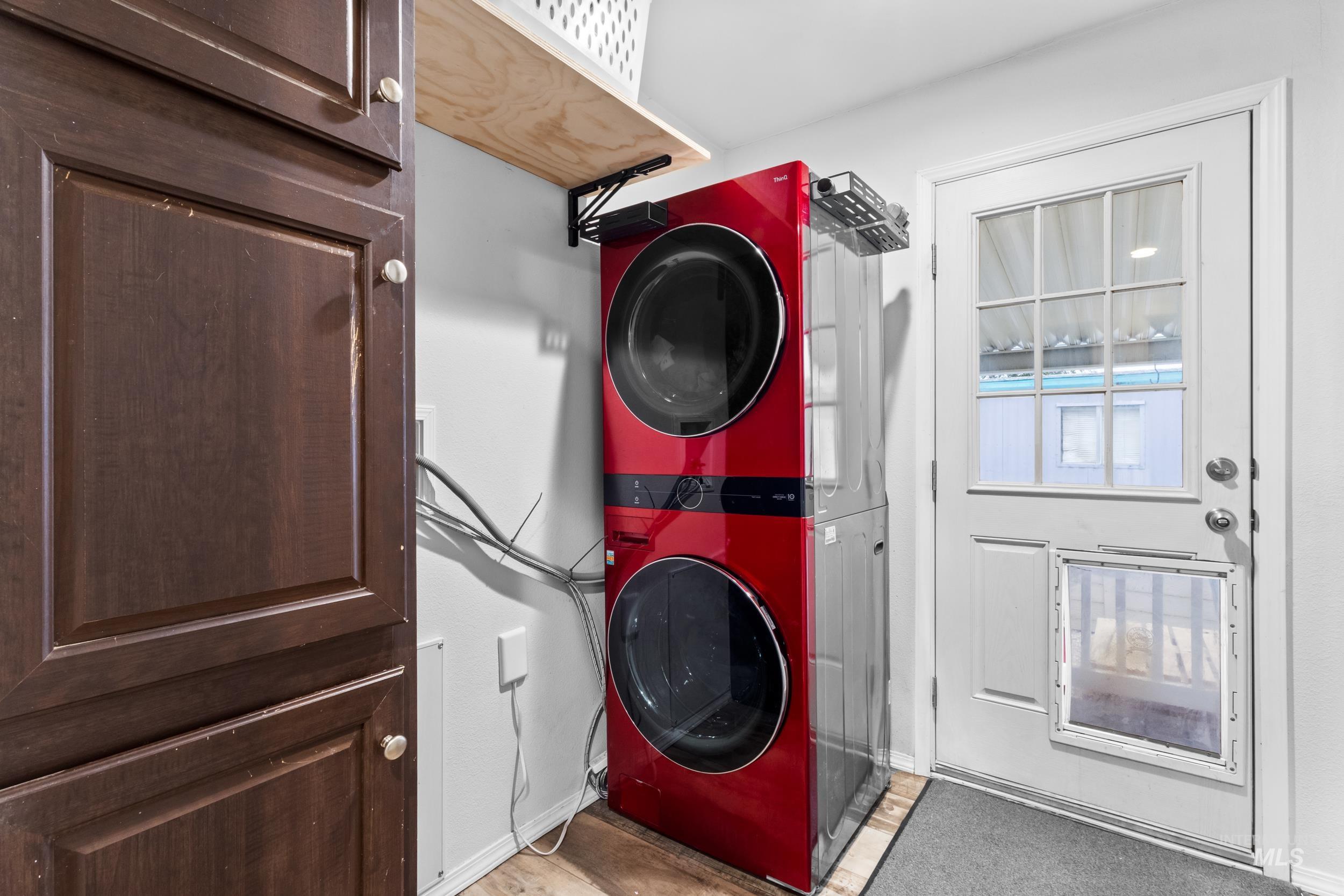Washroom with stacked washer and clothes dryer and wood finished floors