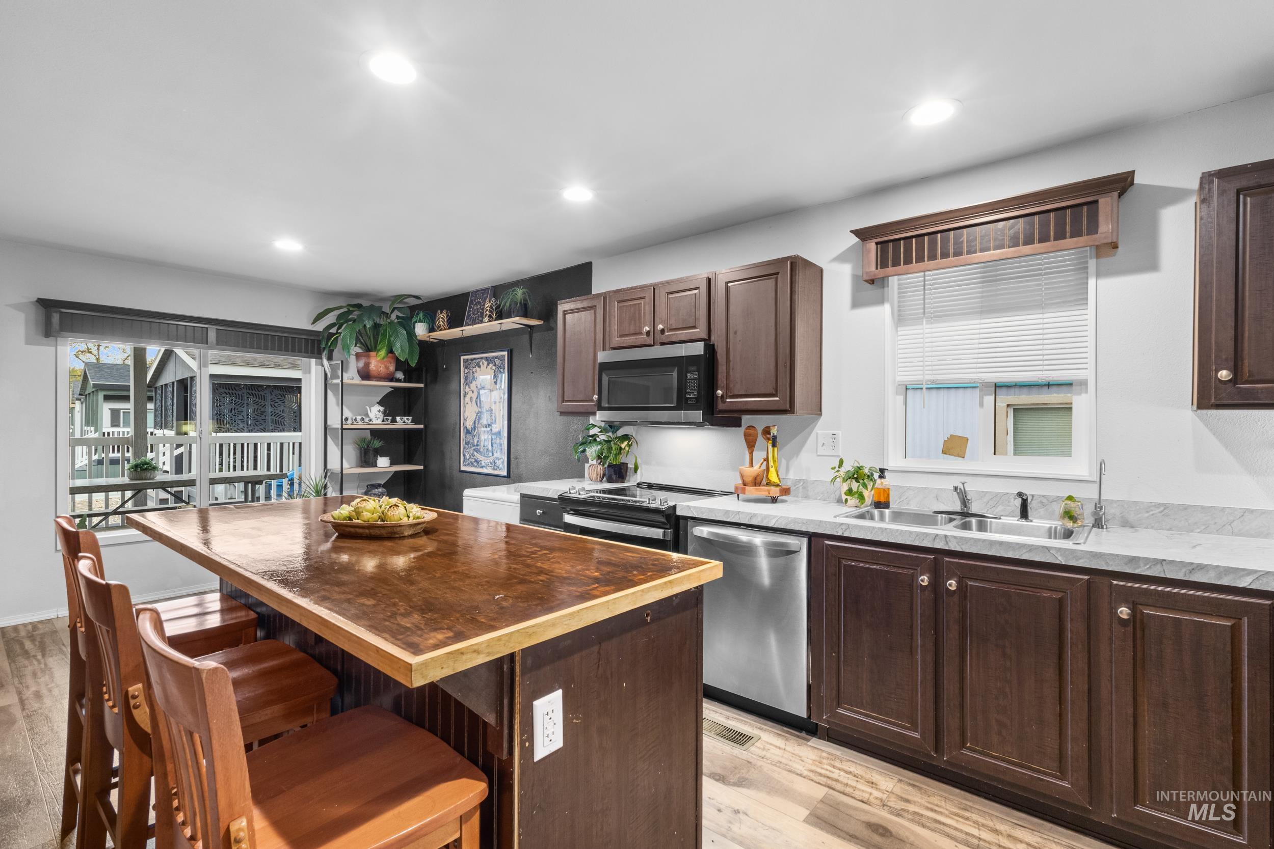 Kitchen with wooden counters, dark brown cabinets, a kitchen island, light wood-style floors, and appliances with stainless steel finishes