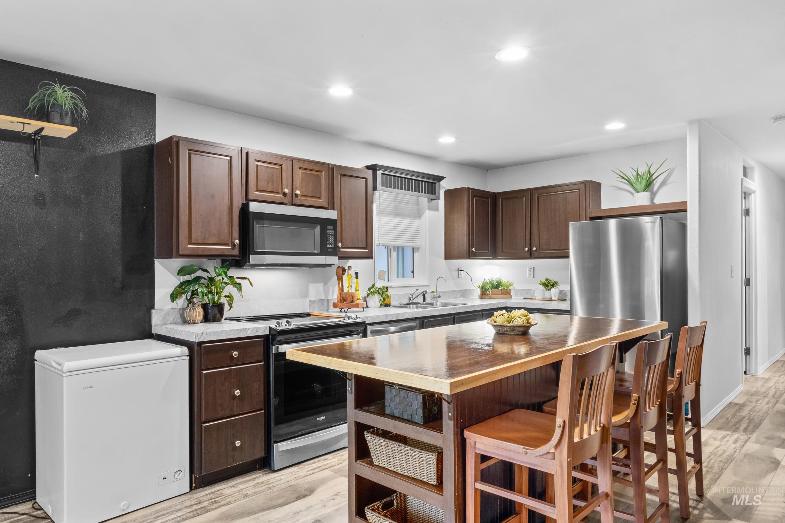 Kitchen featuring dark brown cabinets, appliances with stainless steel finishes, a breakfast bar area, light wood-type flooring, and recessed lighting