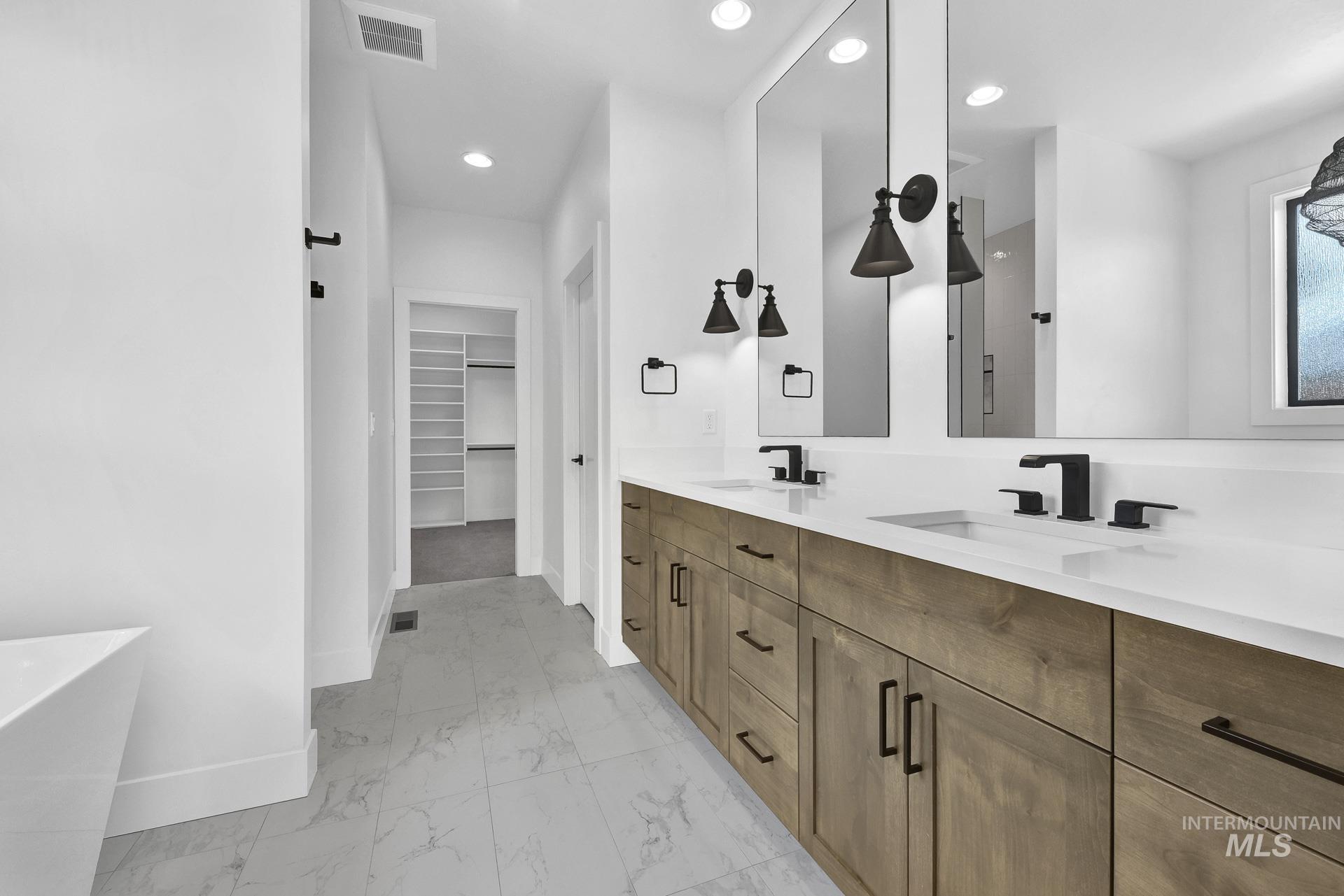Full bathroom with double vanity, a freestanding bath, marble look tile flooring, a walk in closet, and recessed lighting