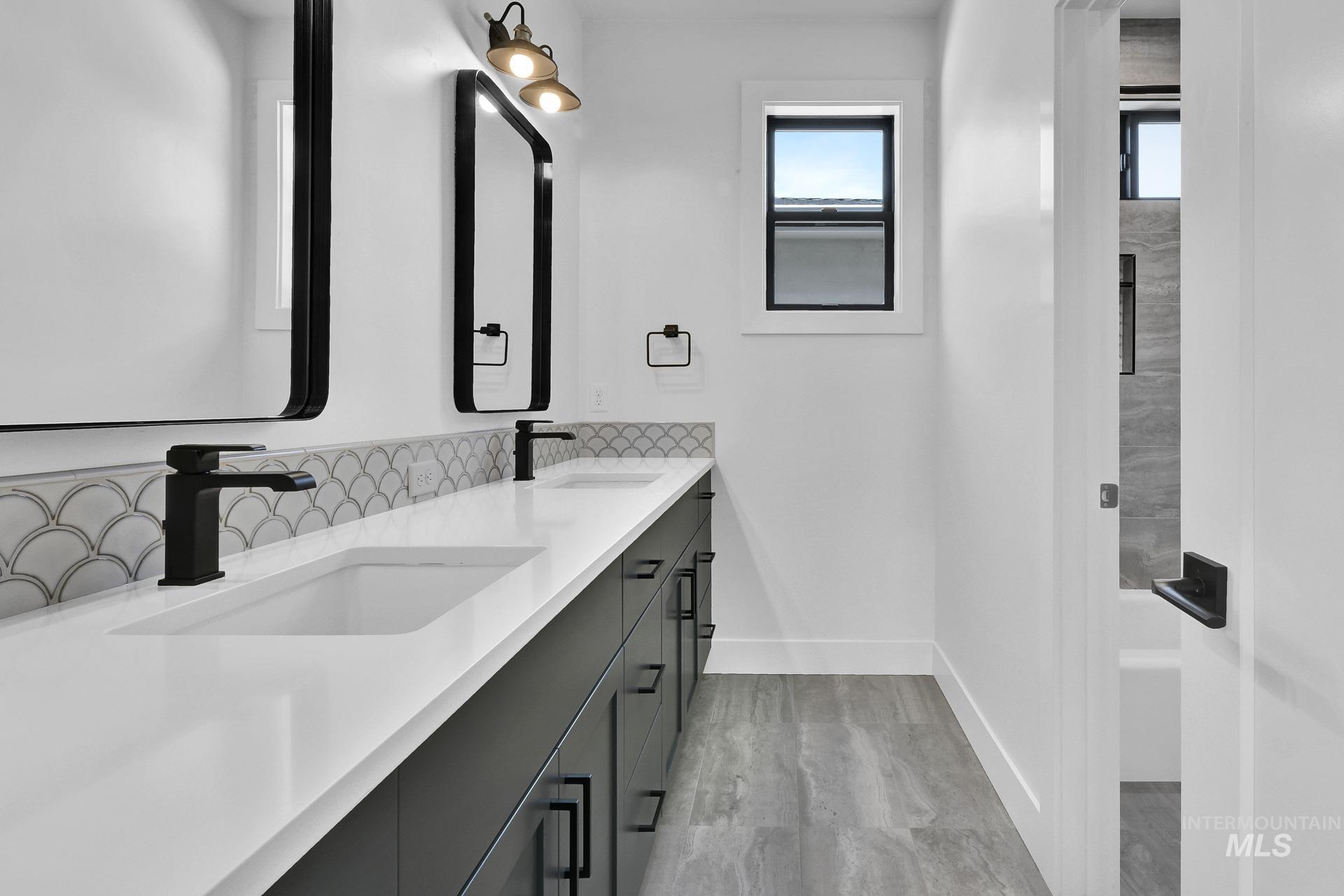 Full bath featuring double vanity, light wood-style flooring, and tasteful backsplash