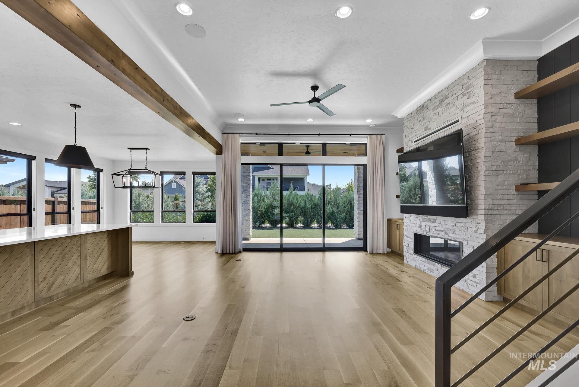 Unfurnished living room with a stone fireplace, healthy amount of natural light, a ceiling fan, light wood-style floors, and ornamental molding