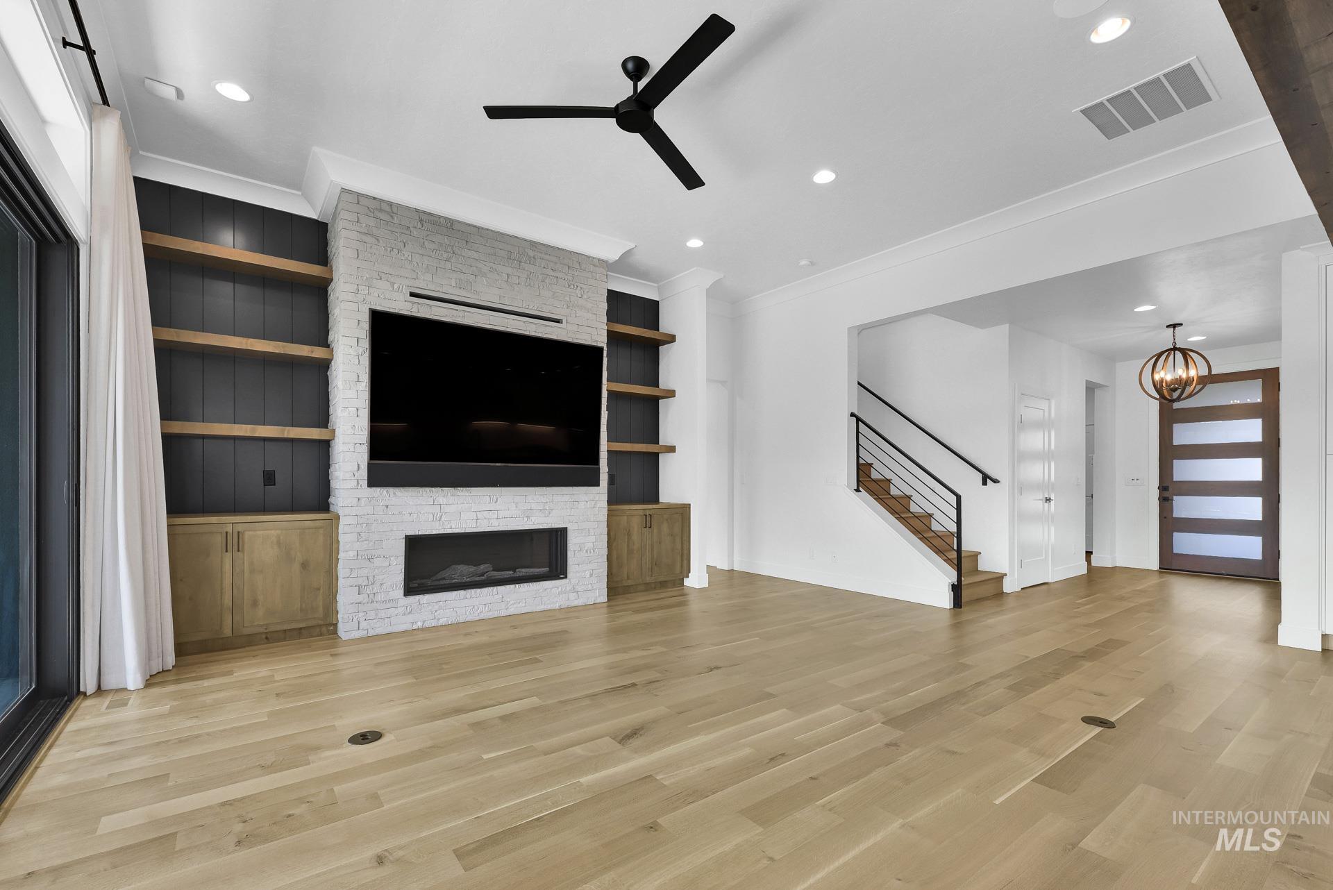Unfurnished living room with ceiling fan, stairs, crown molding, light wood-style floors, and a stone fireplace
