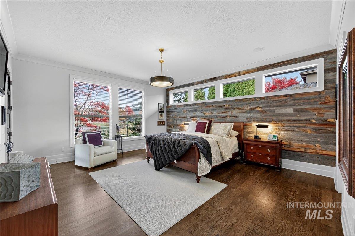 Bedroom with a textured ceiling, an accent wall, dark wood finished floors, crown molding, and wood walls