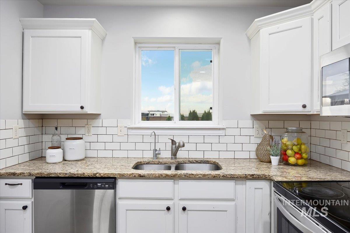 Kitchen featuring white cabinets, stainless steel appliances, light stone countertops, and decorative backsplash