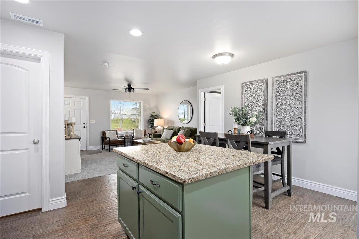 Kitchen featuring green cabinetry, a center island, dark wood-style flooring, light stone counters, and recessed lighting