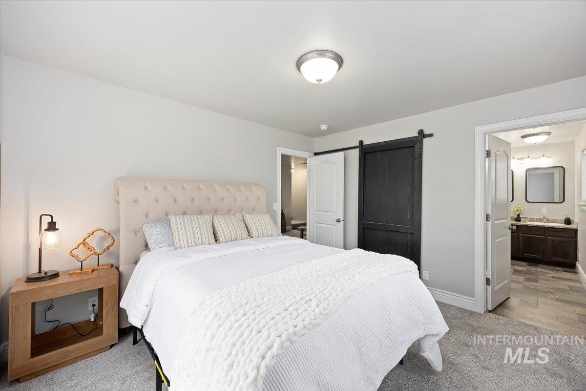 Bedroom featuring a barn door, light colored carpet, and ensuite bath