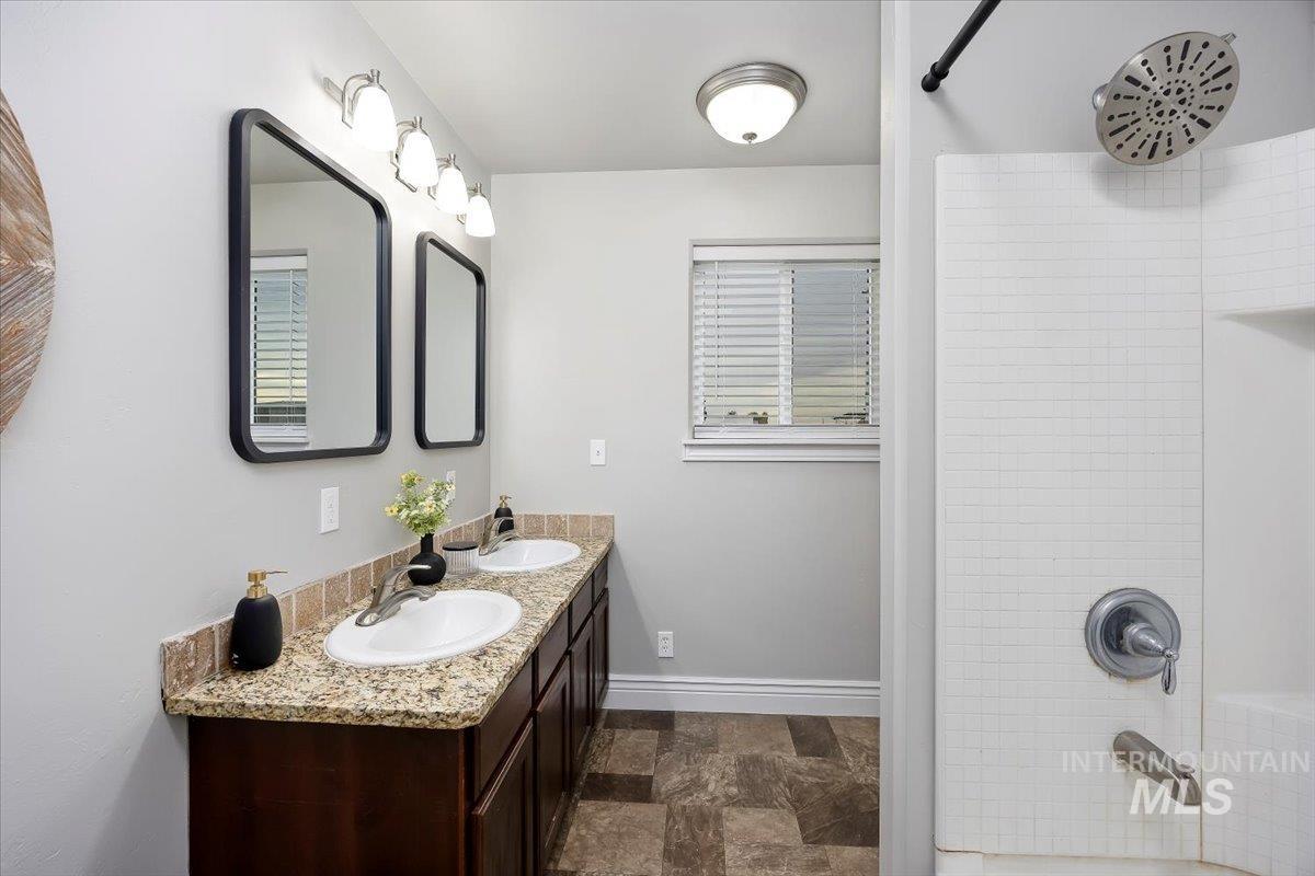 Full bathroom with double vanity, washtub / shower combination, and stone finish flooring