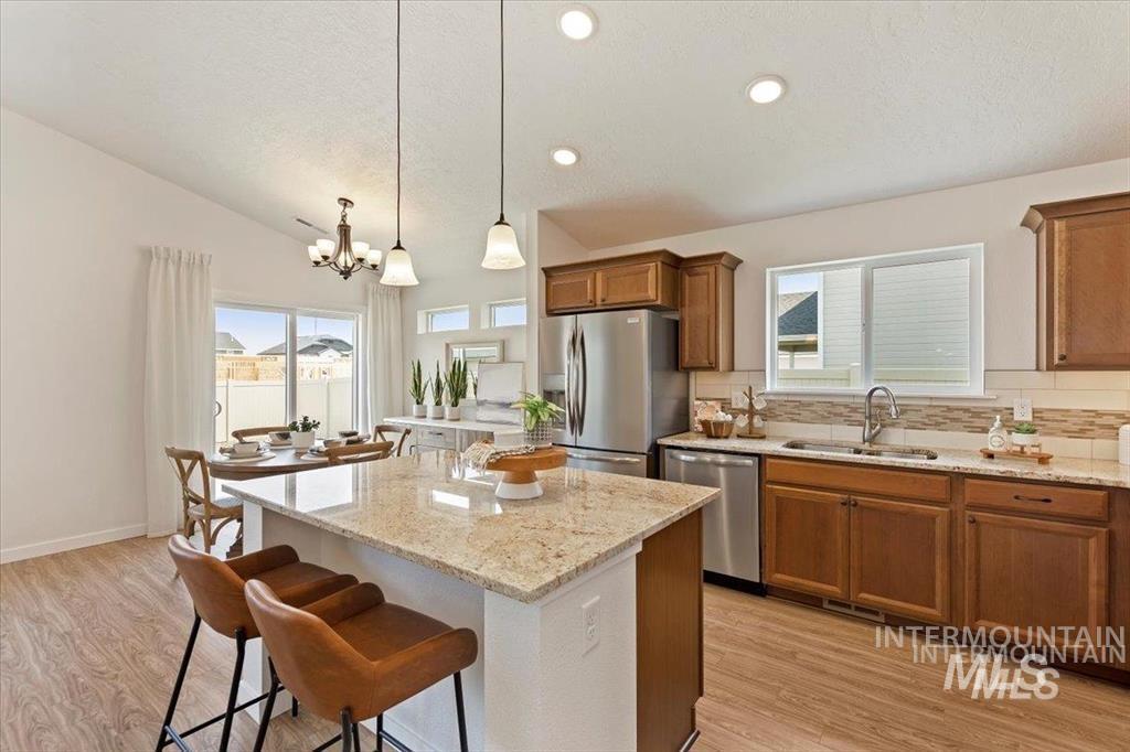 Kitchen featuring brown cabinets, a breakfast bar, light wood-style flooring, light stone counters, and decorative backsplash