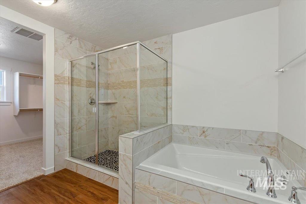 Full bath featuring a textured ceiling, a garden tub, a shower stall, a spacious closet, and wood finished floors