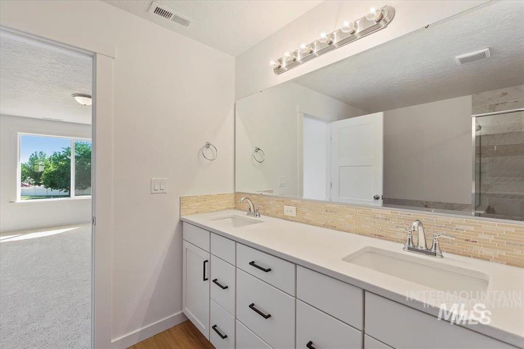Full bathroom featuring double vanity, tasteful backsplash, tiled shower, and a textured ceiling