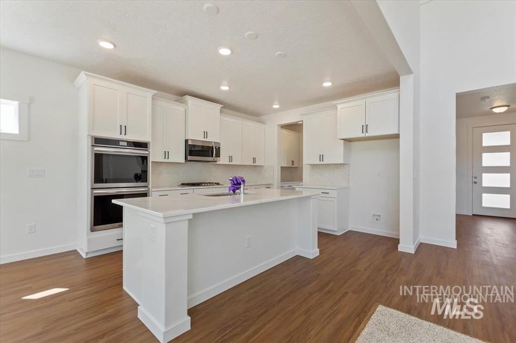 Kitchen with appliances with stainless steel finishes, white cabinets, a kitchen island with sink, dark wood finished floors, and recessed lighting