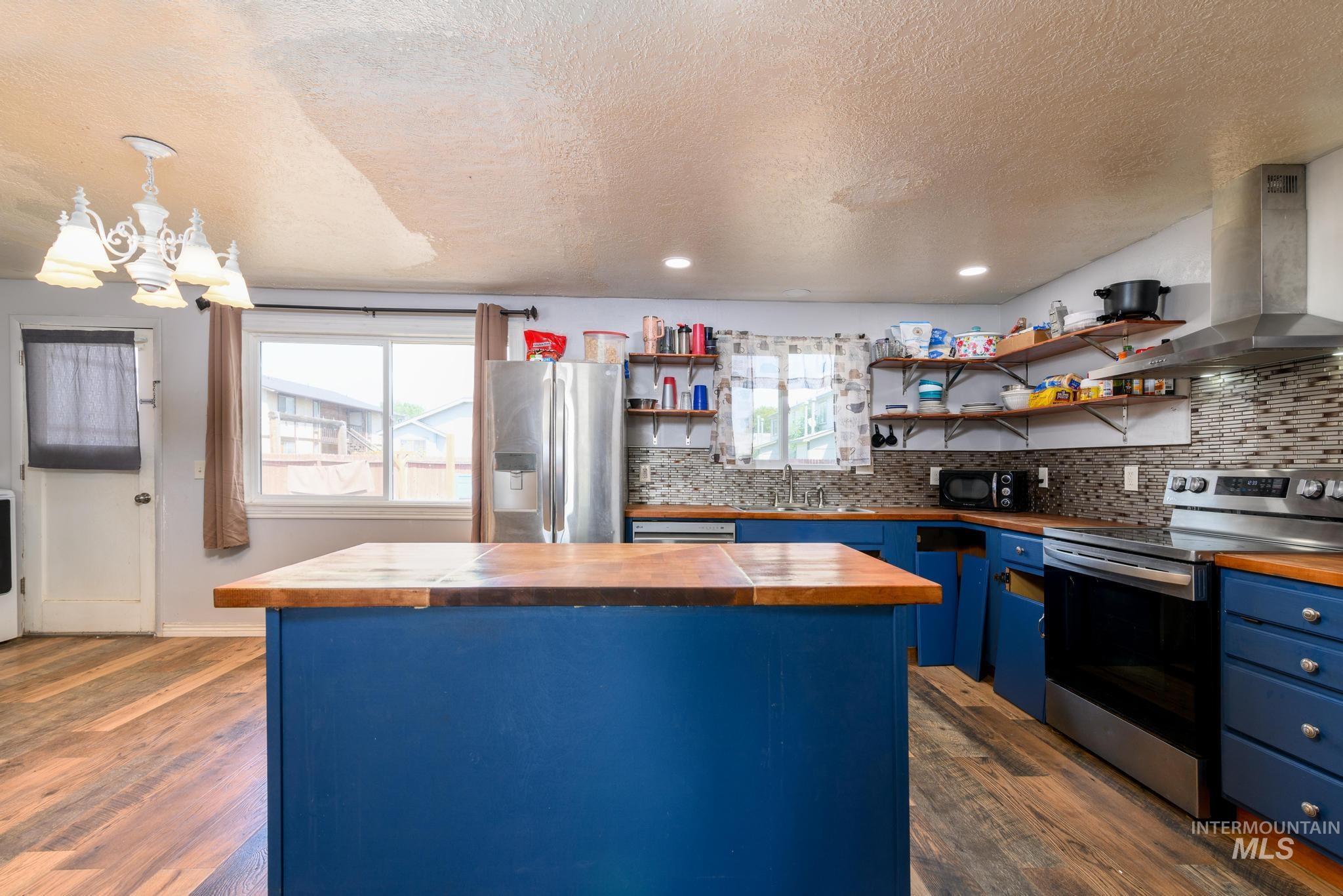 Kitchen featuring blue cabinets, a center island, appliances with stainless steel finishes, butcher block countertops, and dark wood-type flooring