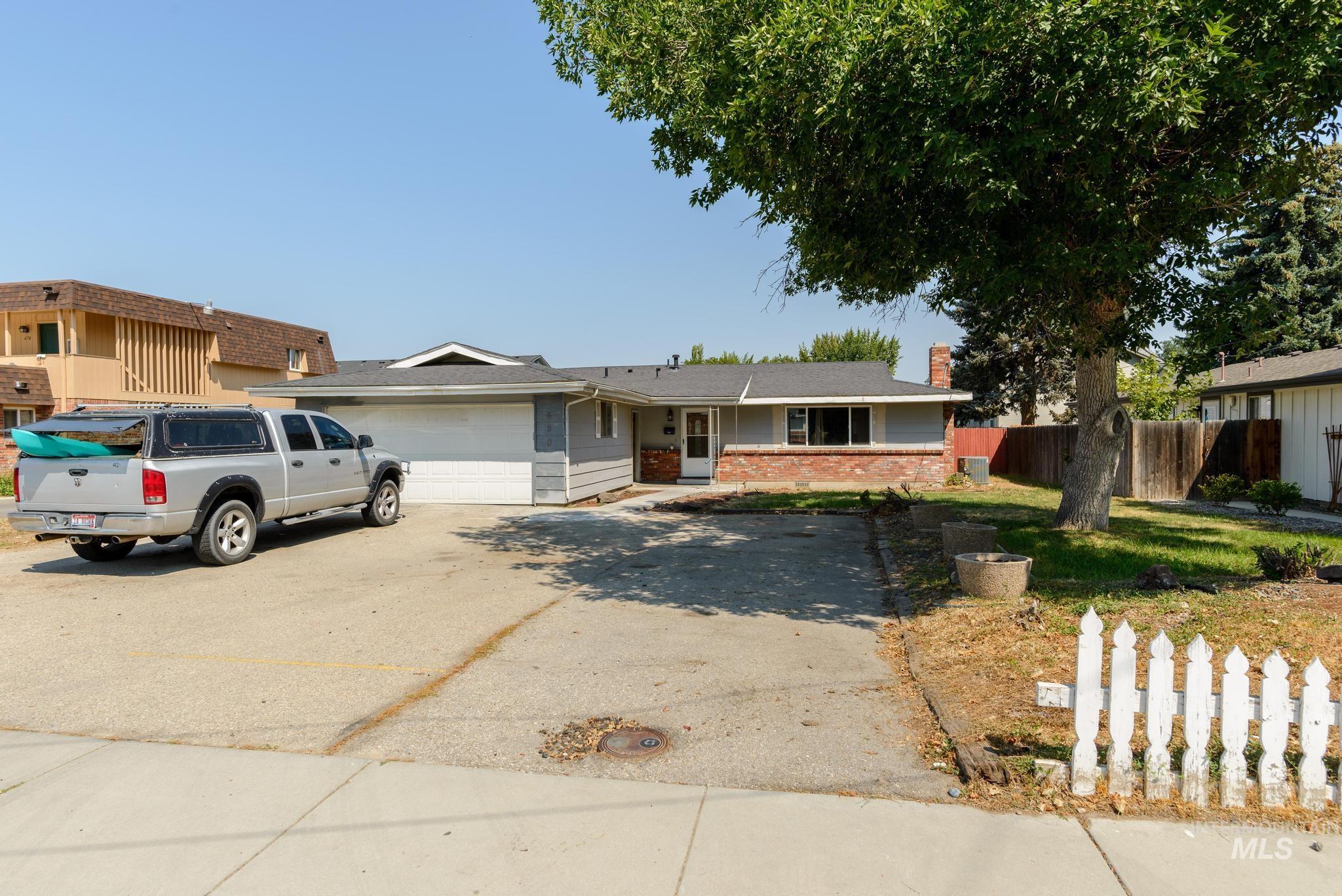 Single story home featuring driveway, brick siding, a chimney, and a garage