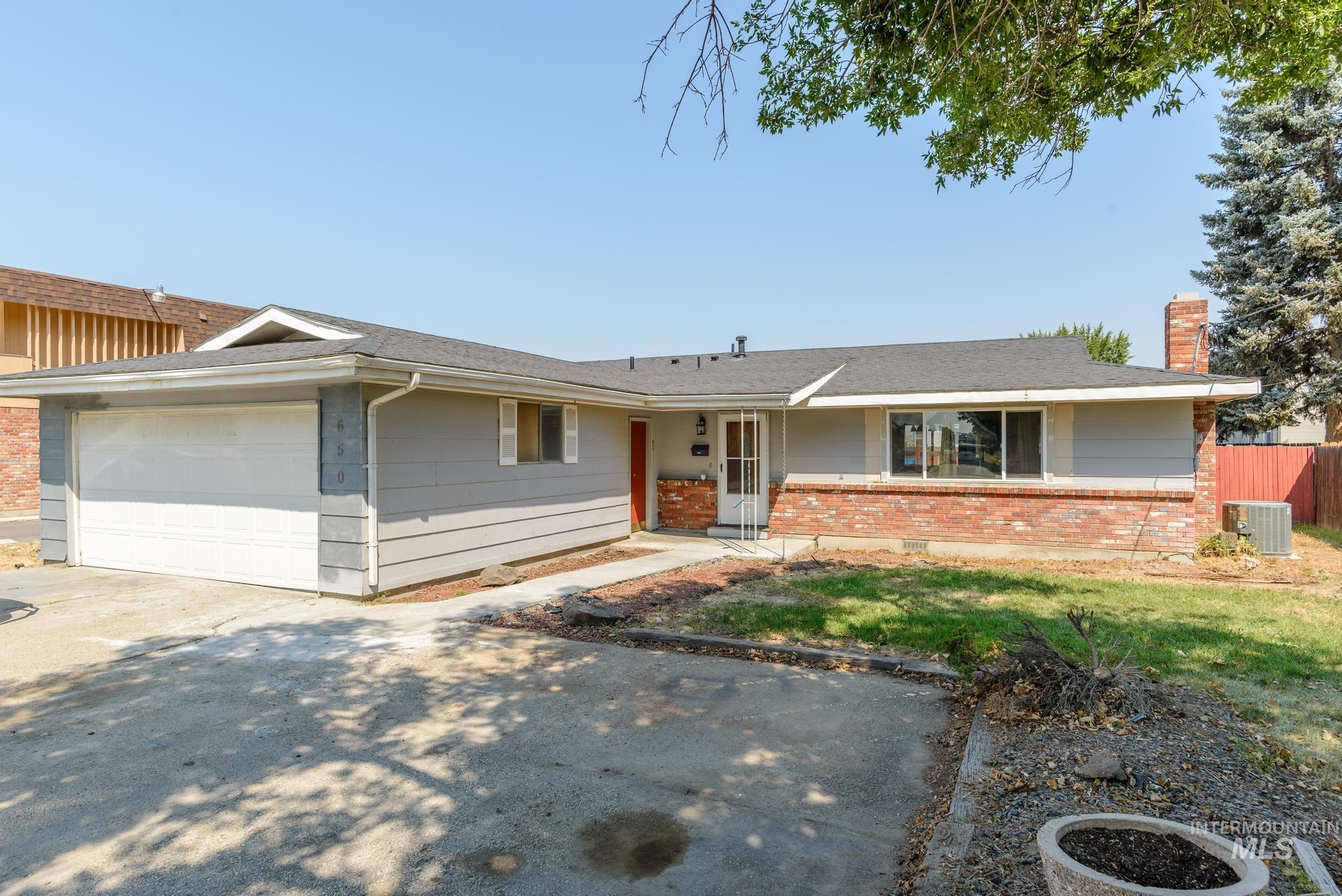 Ranch-style house featuring driveway, brick siding, a garage, and a chimney