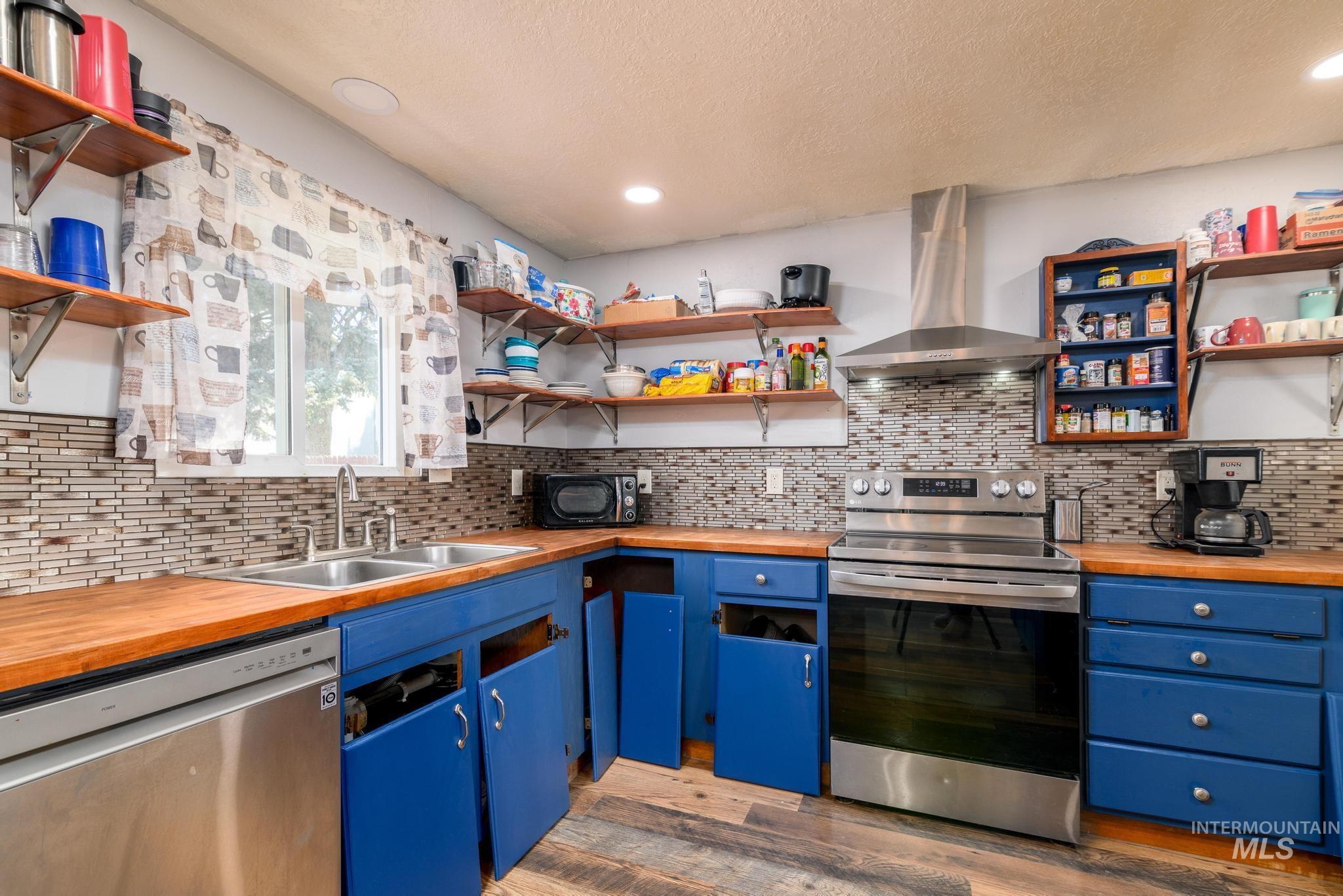 Kitchen featuring wooden counters, appliances with stainless steel finishes, open shelves, a textured ceiling, and blue cabinetry