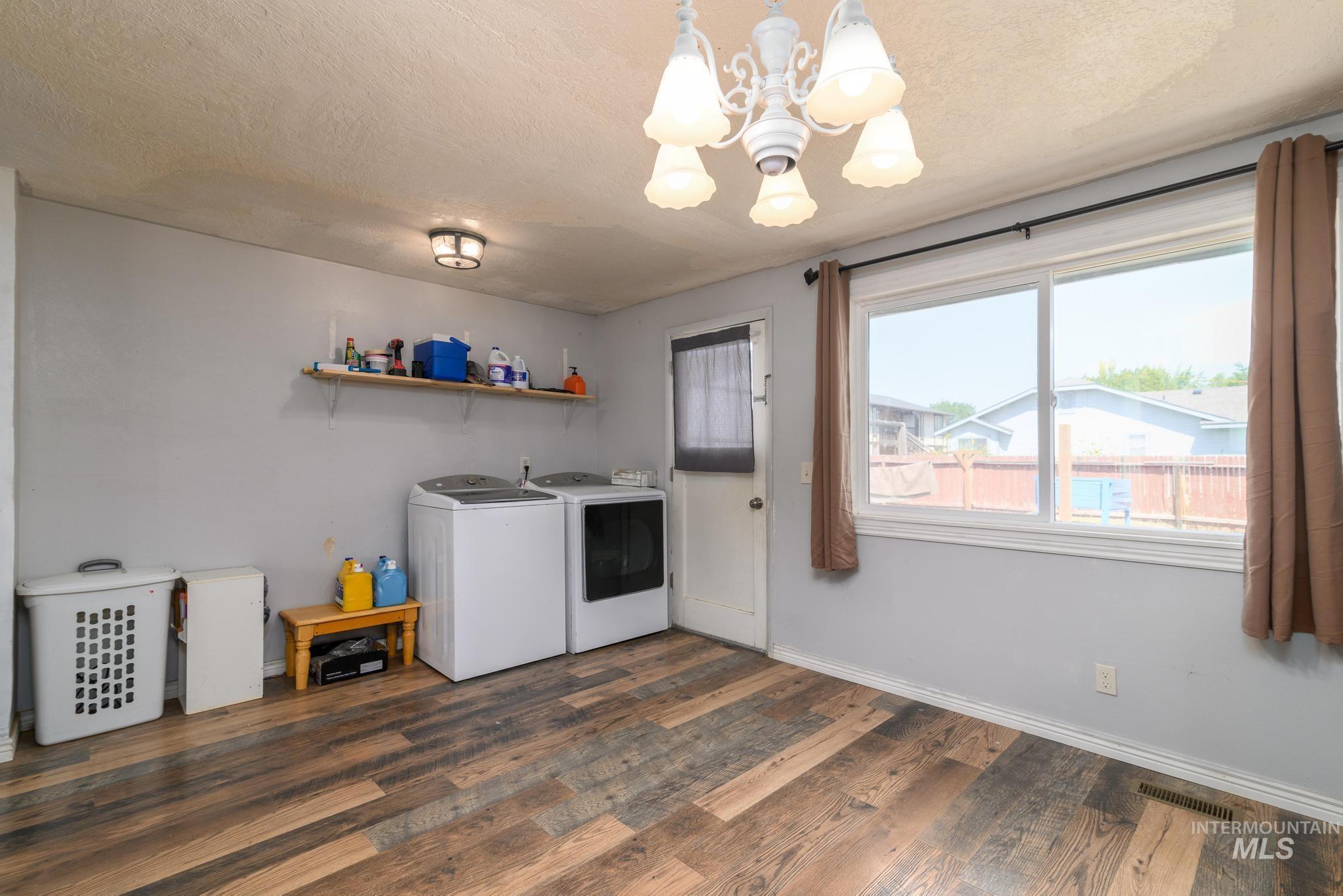 Laundry area featuring a textured ceiling, washer and clothes dryer, dark wood-type flooring, and a chandelier