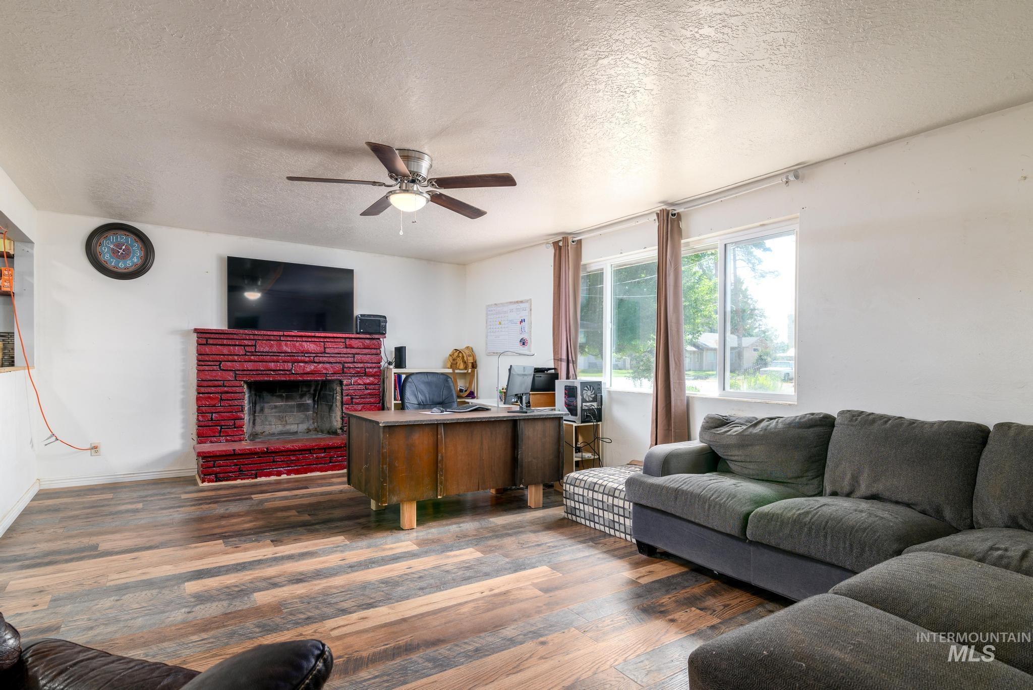 Living room with a textured ceiling, a fireplace, wood finished floors, and ceiling fan