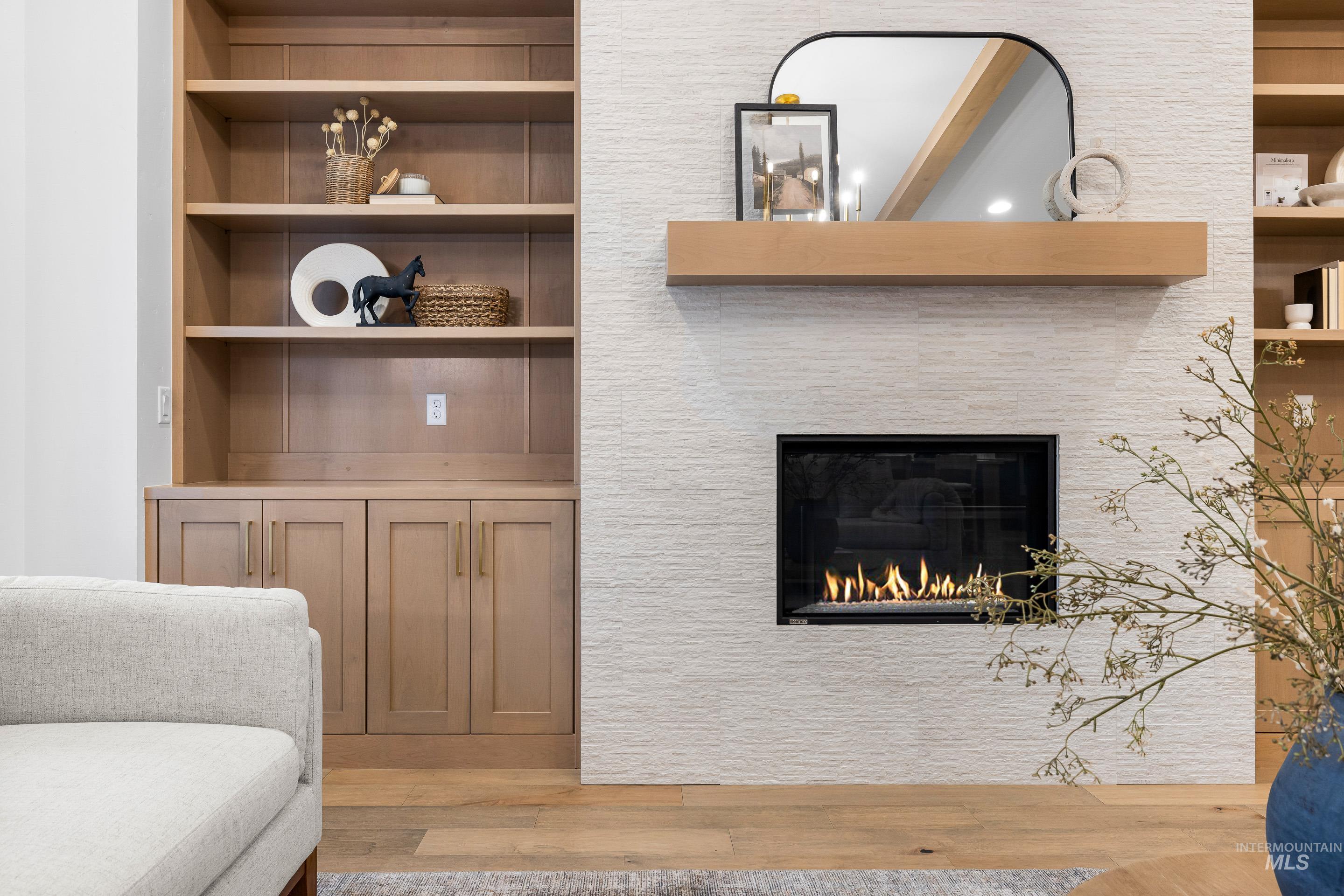 Living area with built in shelves, light wood-style floors, and a glass covered fireplace