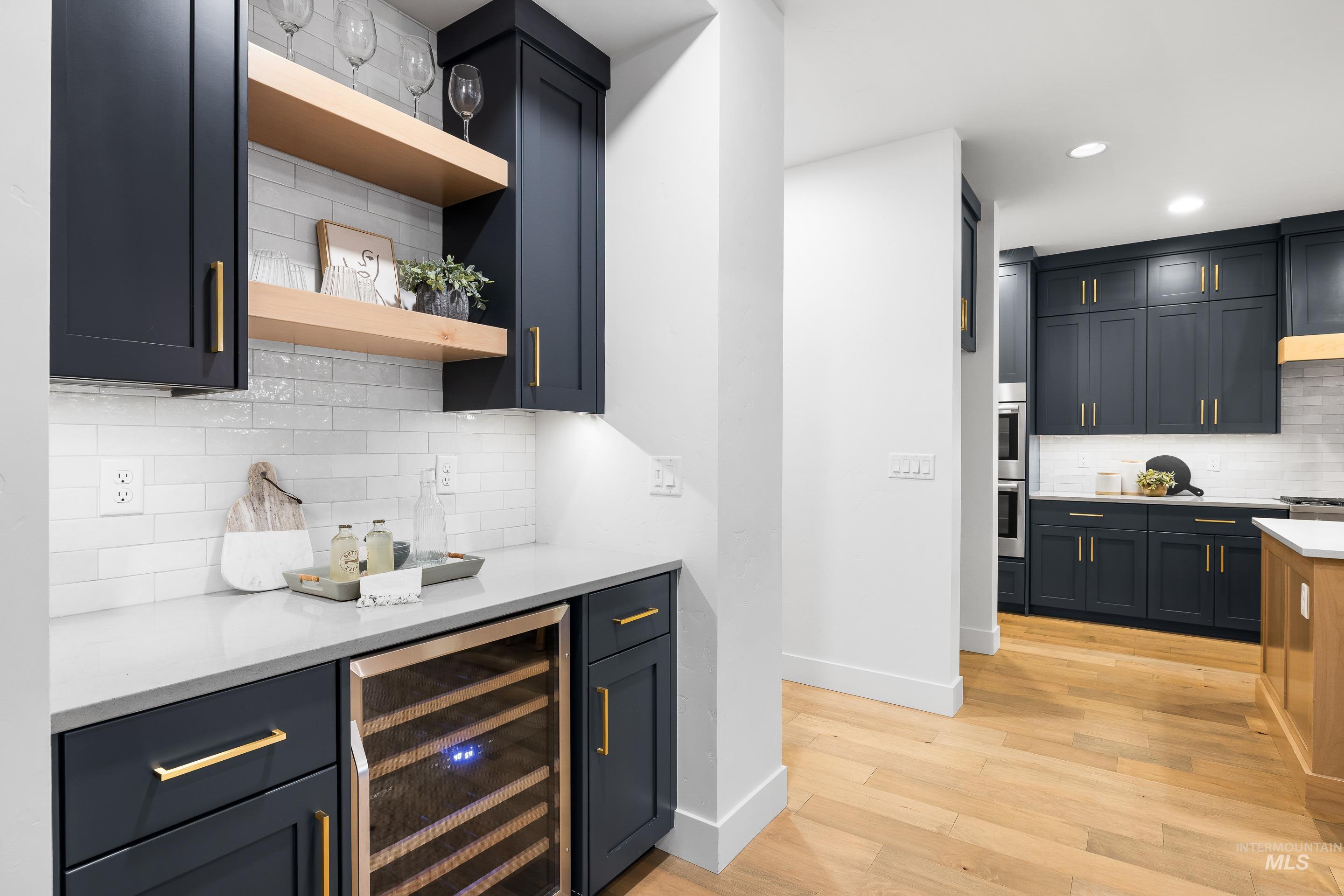 Bar area with backsplash, open shelves, wine cooler, light stone countertops, and light wood-type flooring