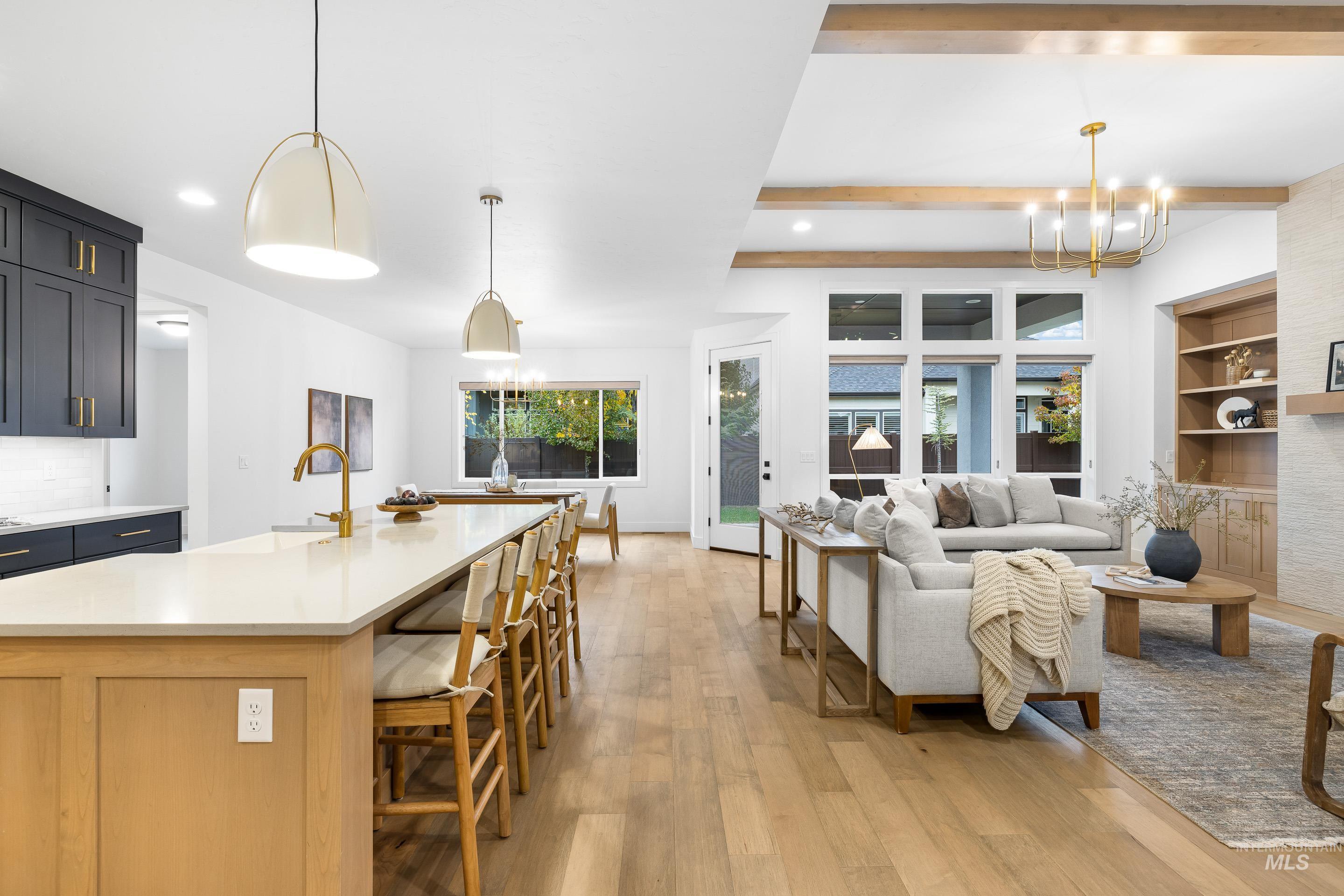 Kitchen with a chandelier, light wood-type flooring, decorative light fixtures, an island with sink, and beam ceiling