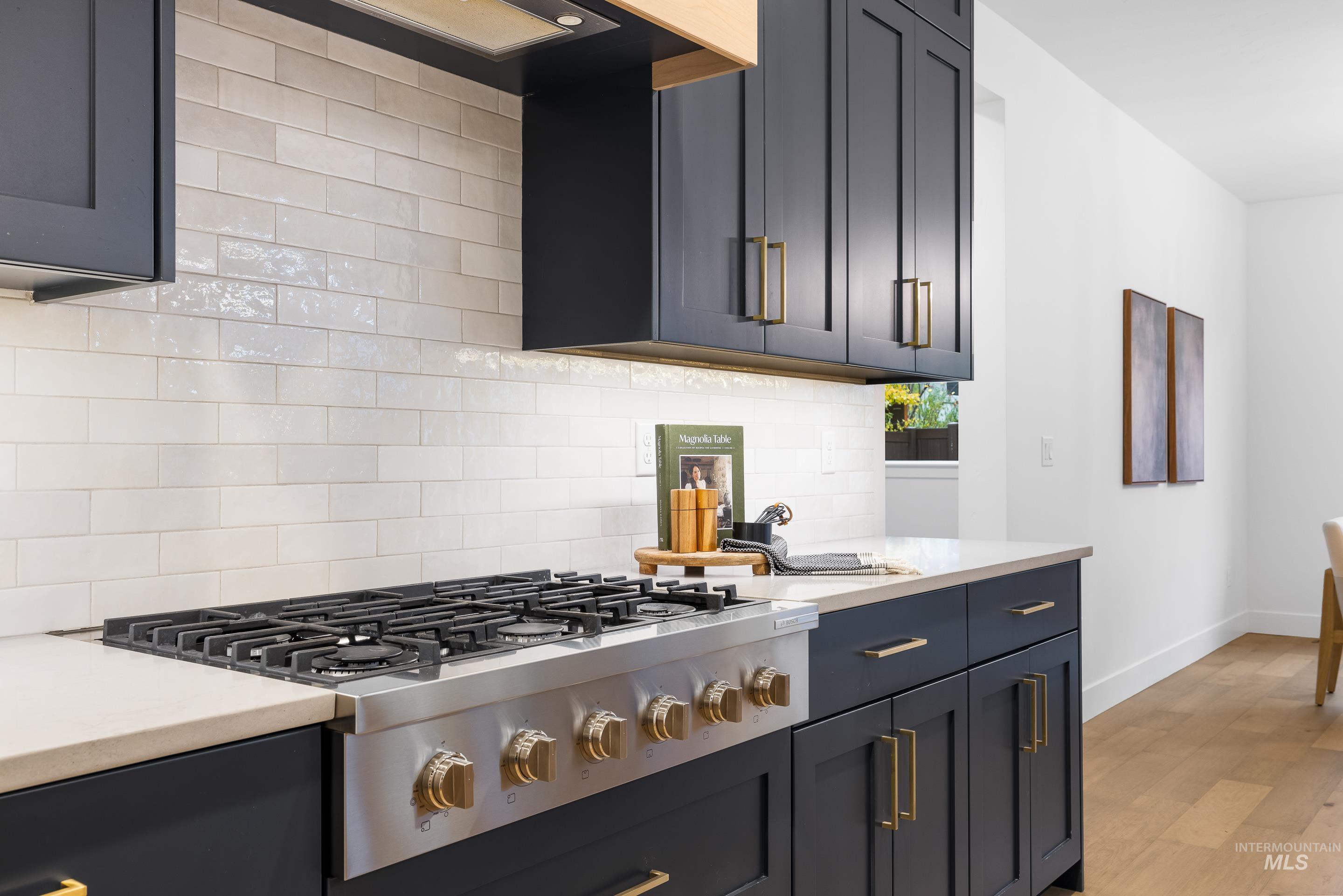 Kitchen featuring stainless steel gas stovetop, light wood-style floors, light stone countertops, backsplash, and range hood