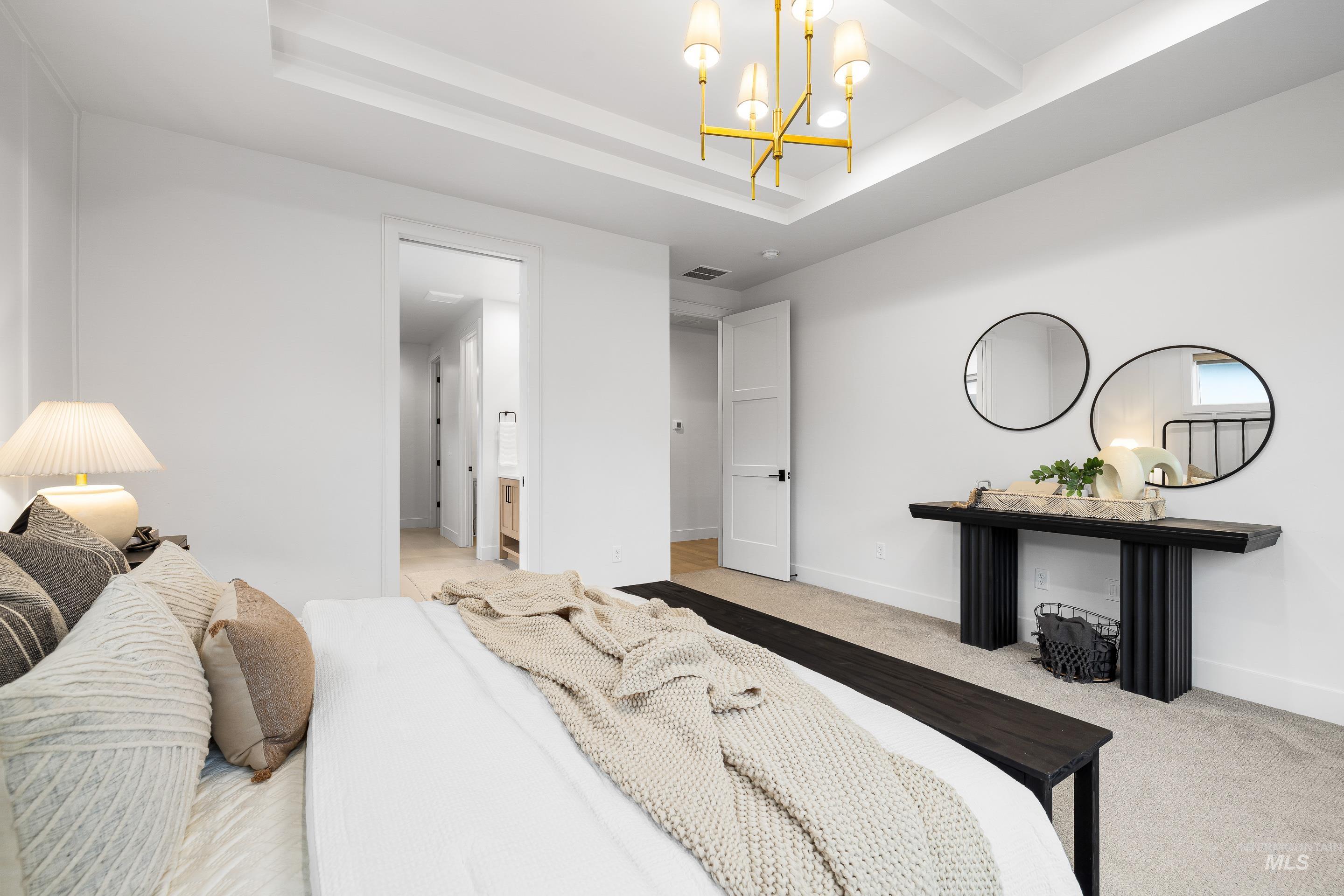 Bedroom with ensuite bath, light colored carpet, a chandelier, and a tray ceiling