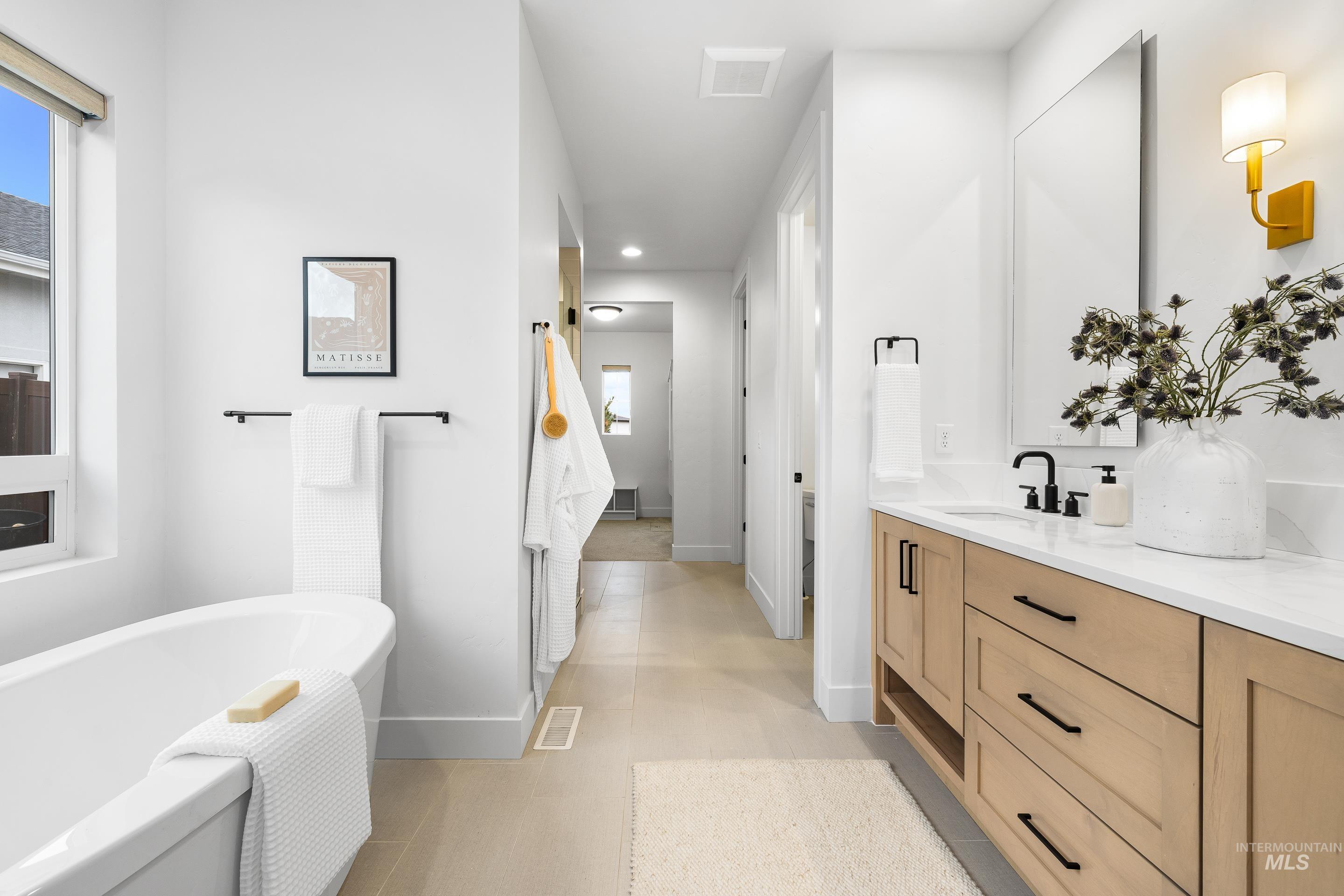 Ensuite bathroom featuring double vanity, a freestanding tub, recessed lighting, and light tile patterned floors