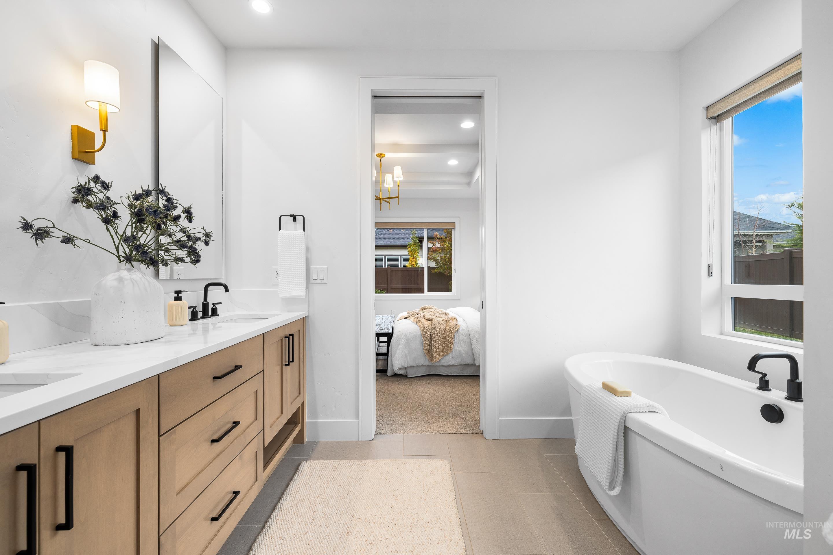 Ensuite bathroom with double vanity, a freestanding tub, recessed lighting, a chandelier, and light tile patterned flooring