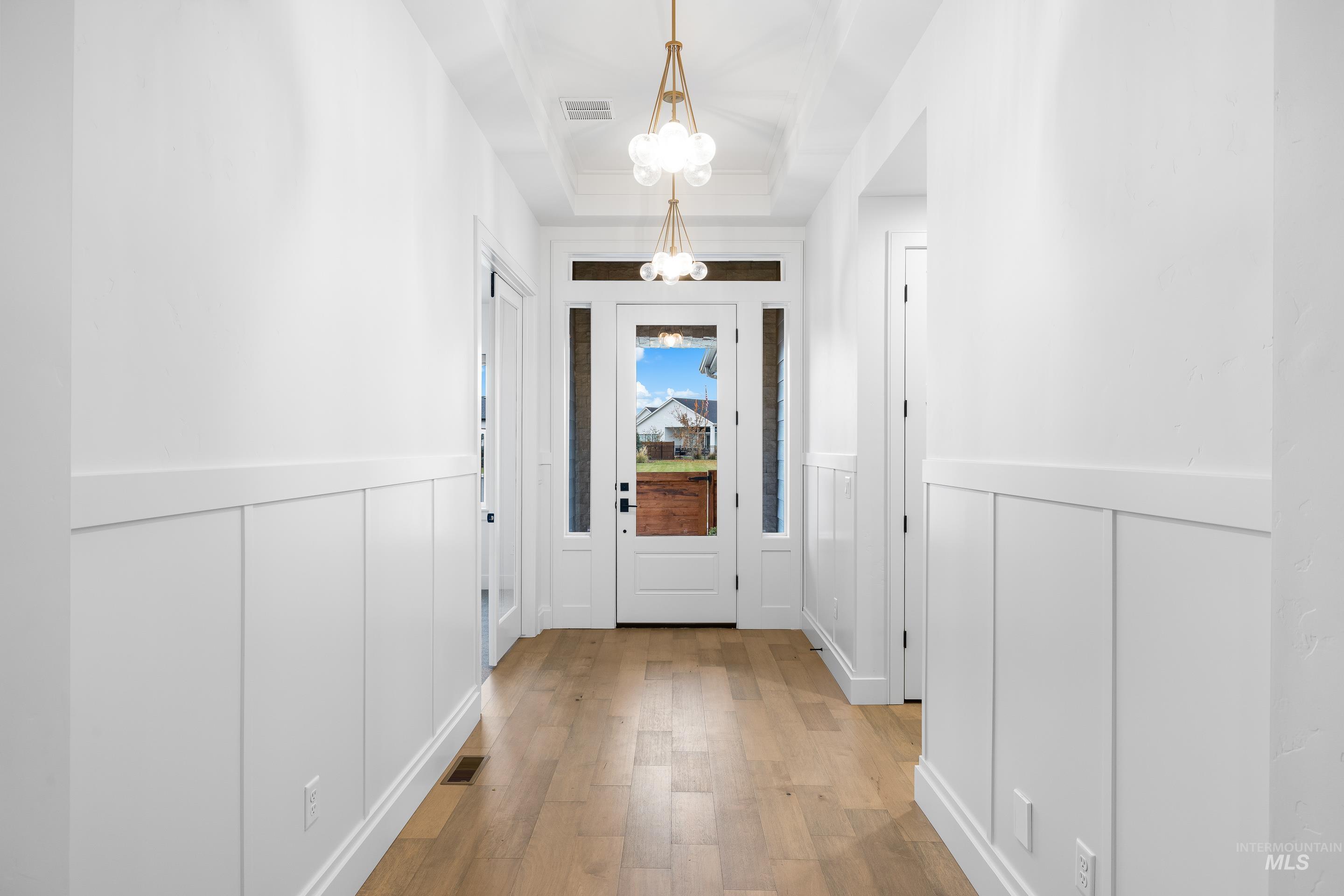 Doorway with a decorative wall, wainscoting, a chandelier, and wood finished floors