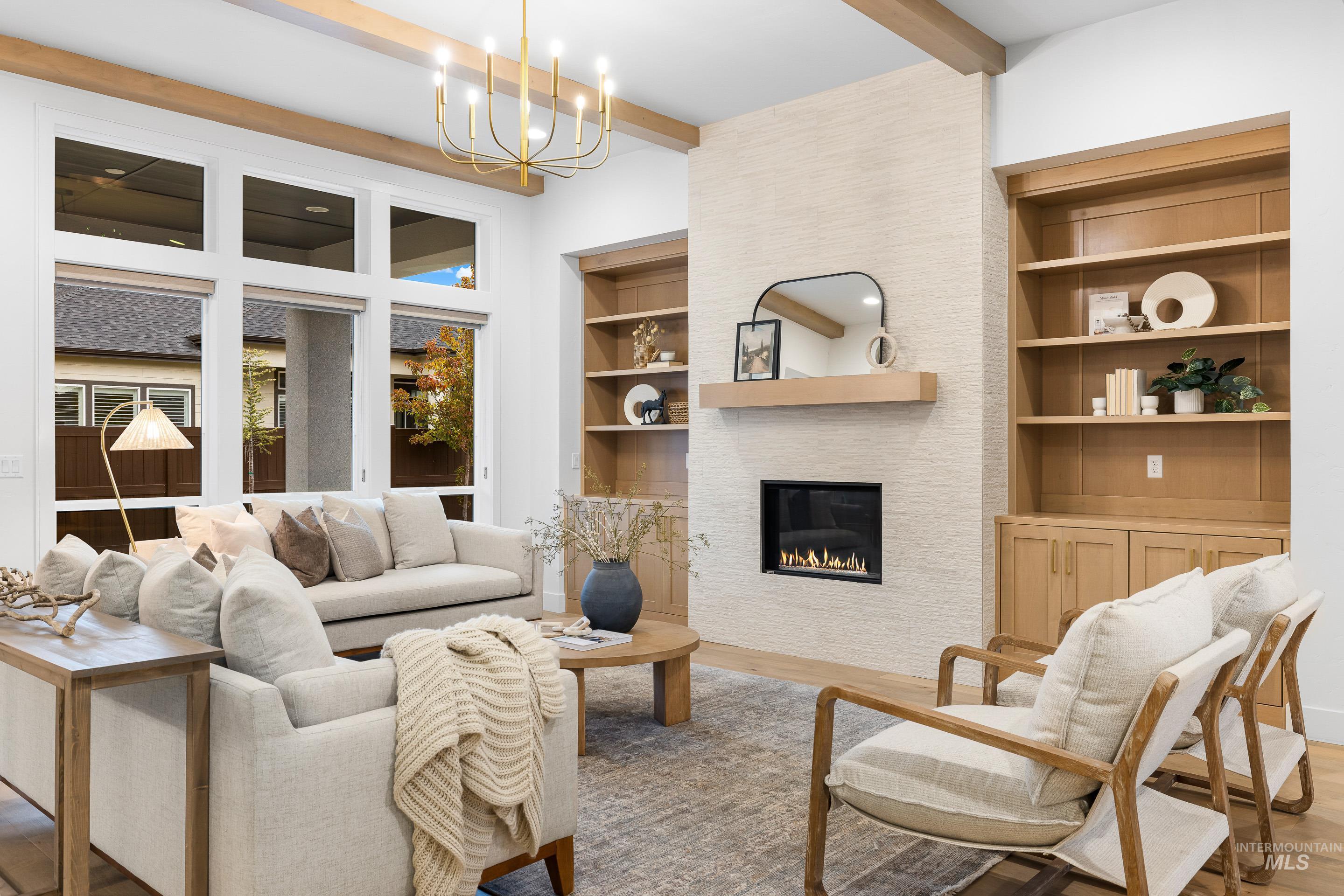 Living area with wood finished floors, beamed ceiling, a large fireplace, and a chandelier
