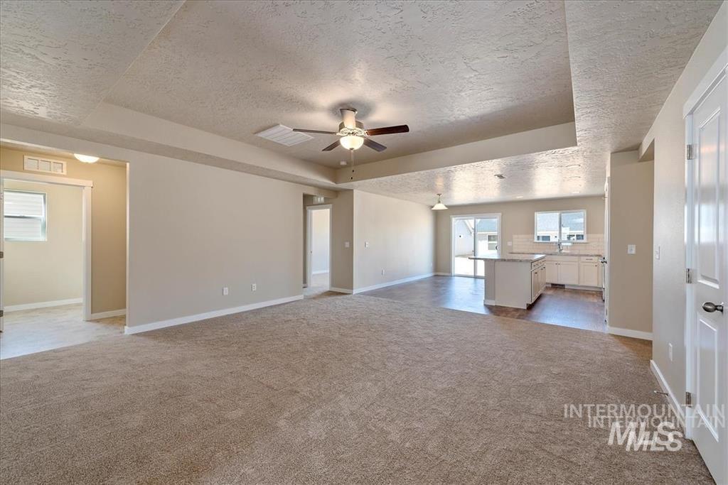 Unfurnished living room featuring a textured ceiling, light carpet, a tray ceiling, and ceiling fan