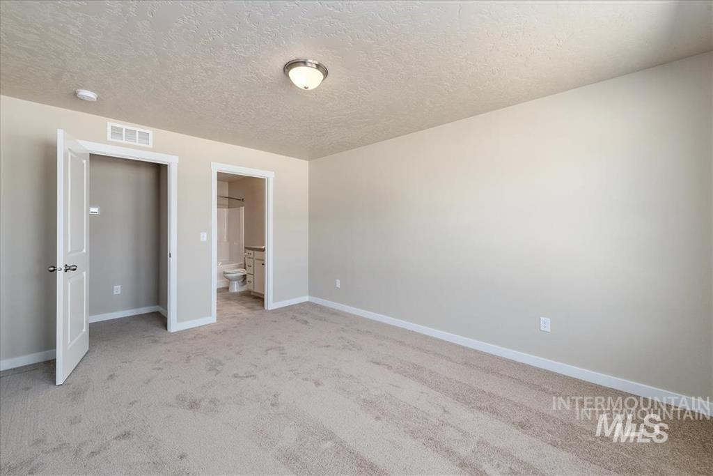 Unfurnished bedroom featuring light carpet, a textured ceiling, and ensuite bathroom