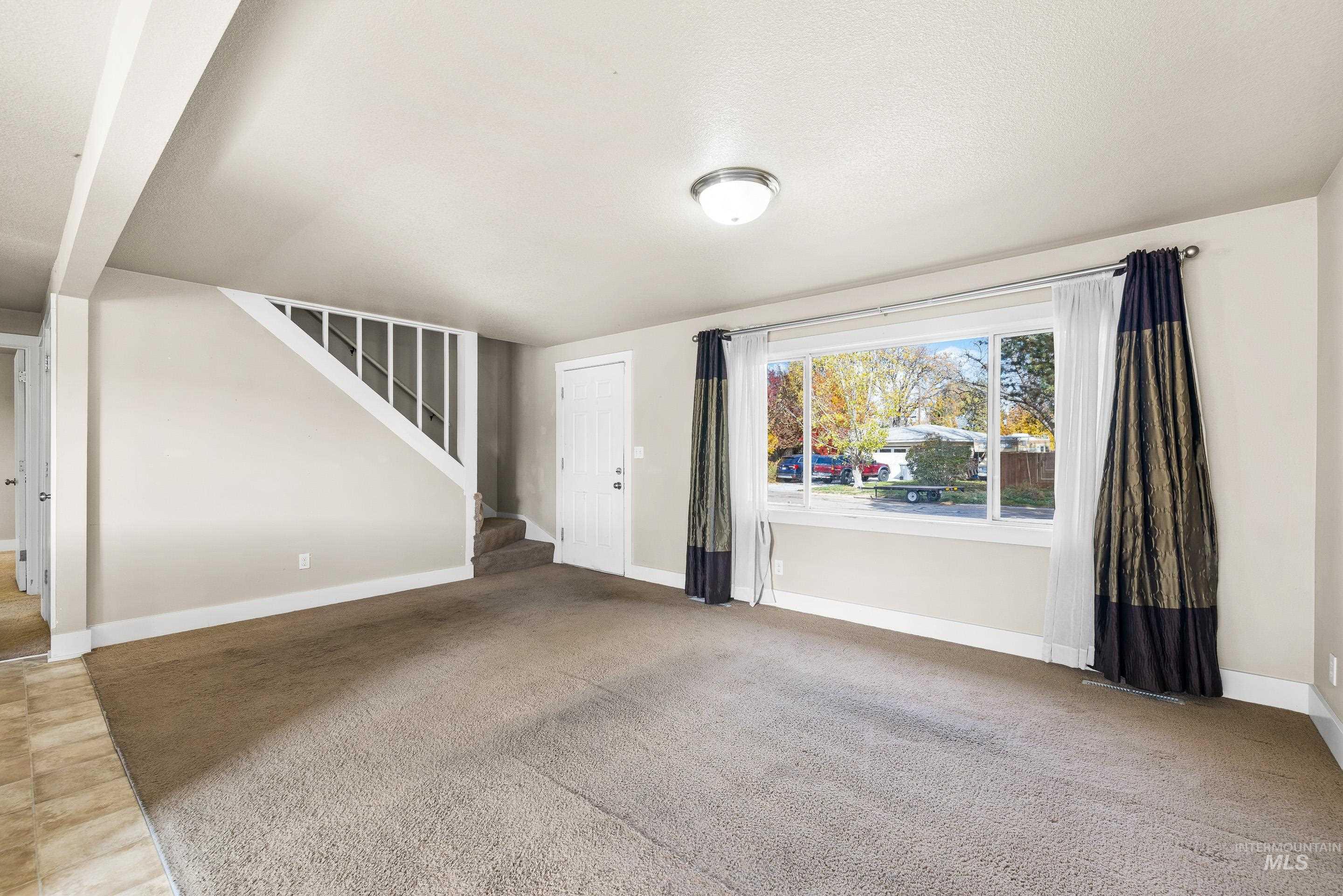 Unfurnished living room with stairway and light colored carpet