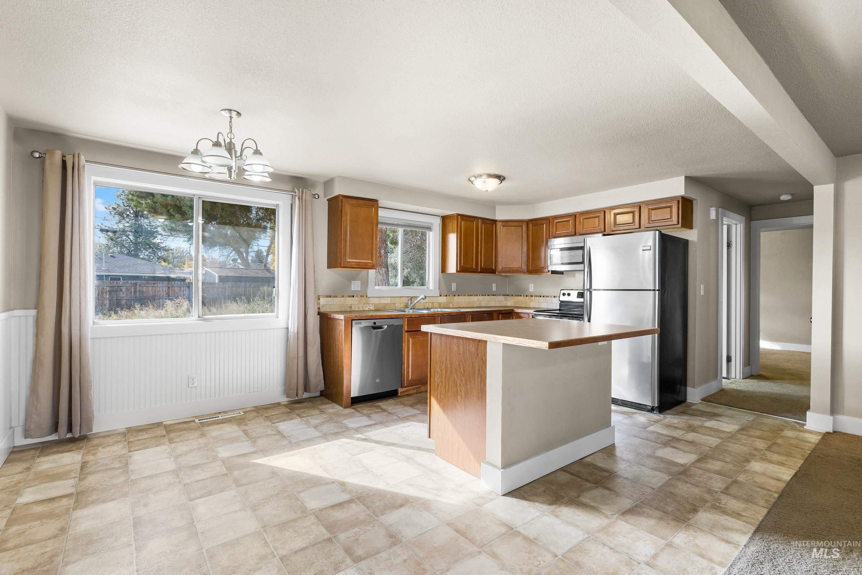 Kitchen with brown cabinets, stainless steel appliances, light countertops, decorative light fixtures, and a chandelier