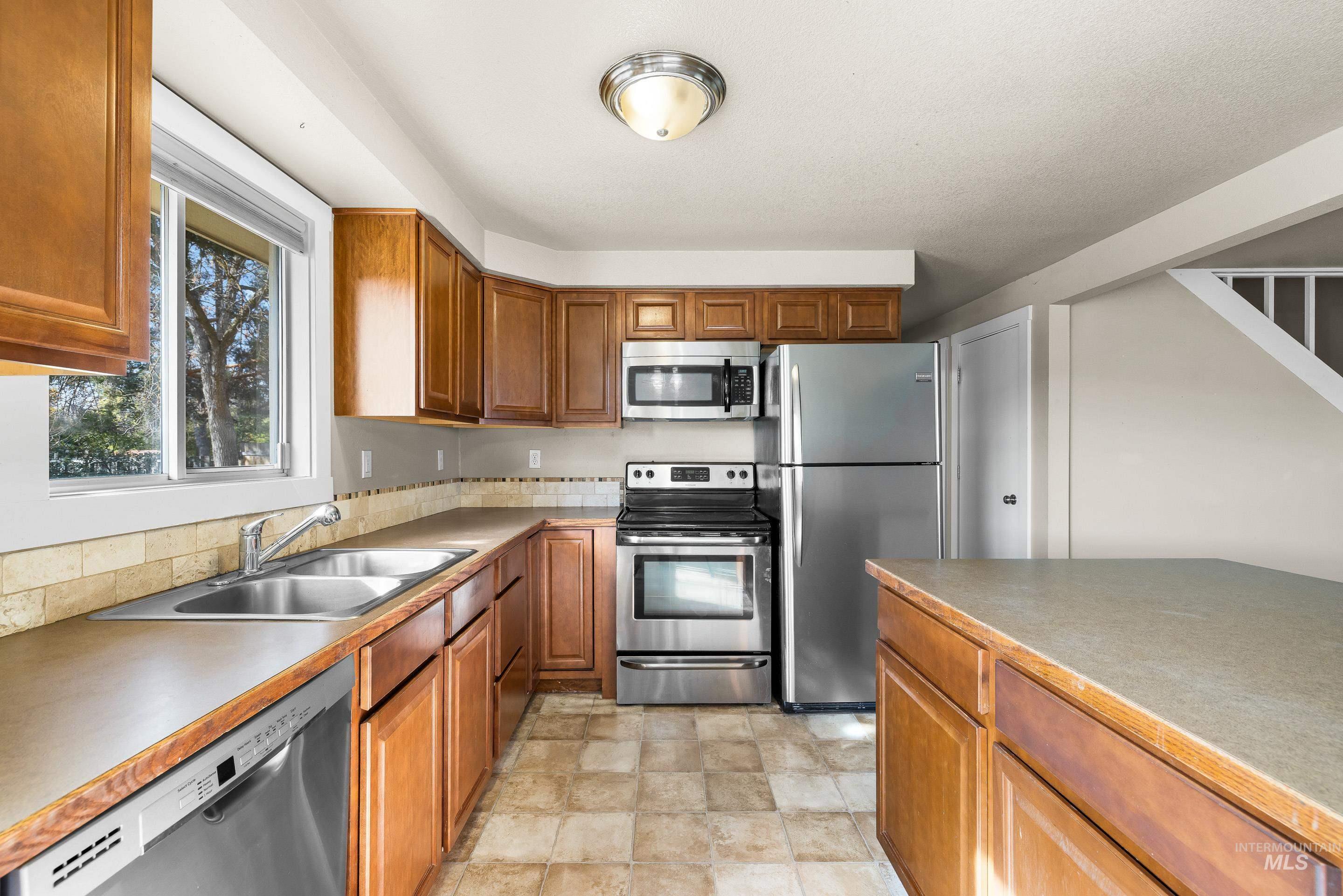 Kitchen with appliances with stainless steel finishes, brown cabinets, stone finish floors, and light countertops