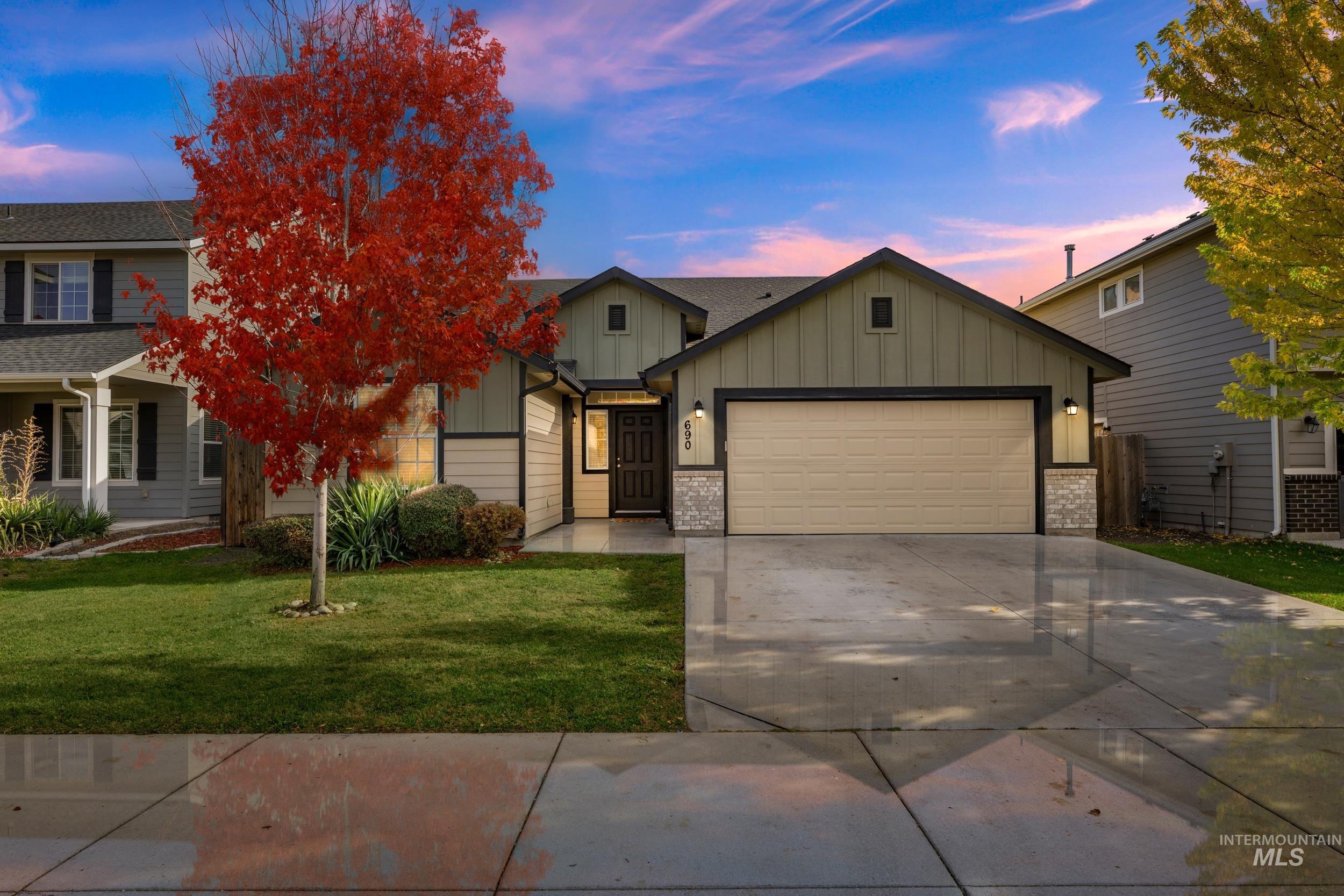 View of front facade with board and batten siding, concrete driveway, a yard, a garage, and brick siding