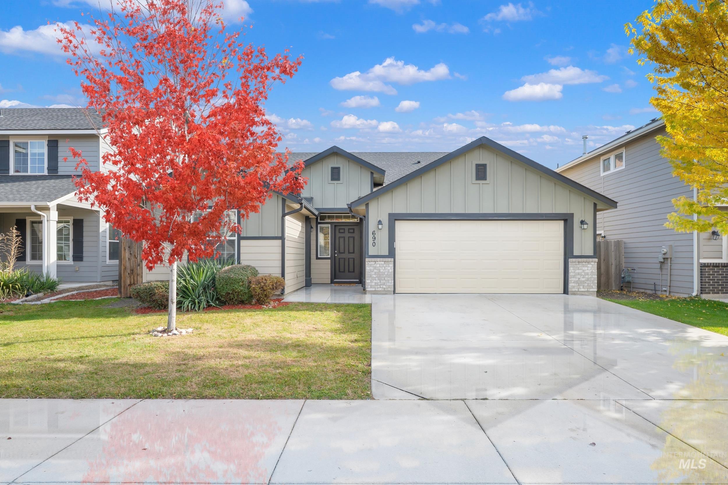 View of front of home featuring board and batten siding, concrete driveway, a front yard, an attached garage, and brick siding