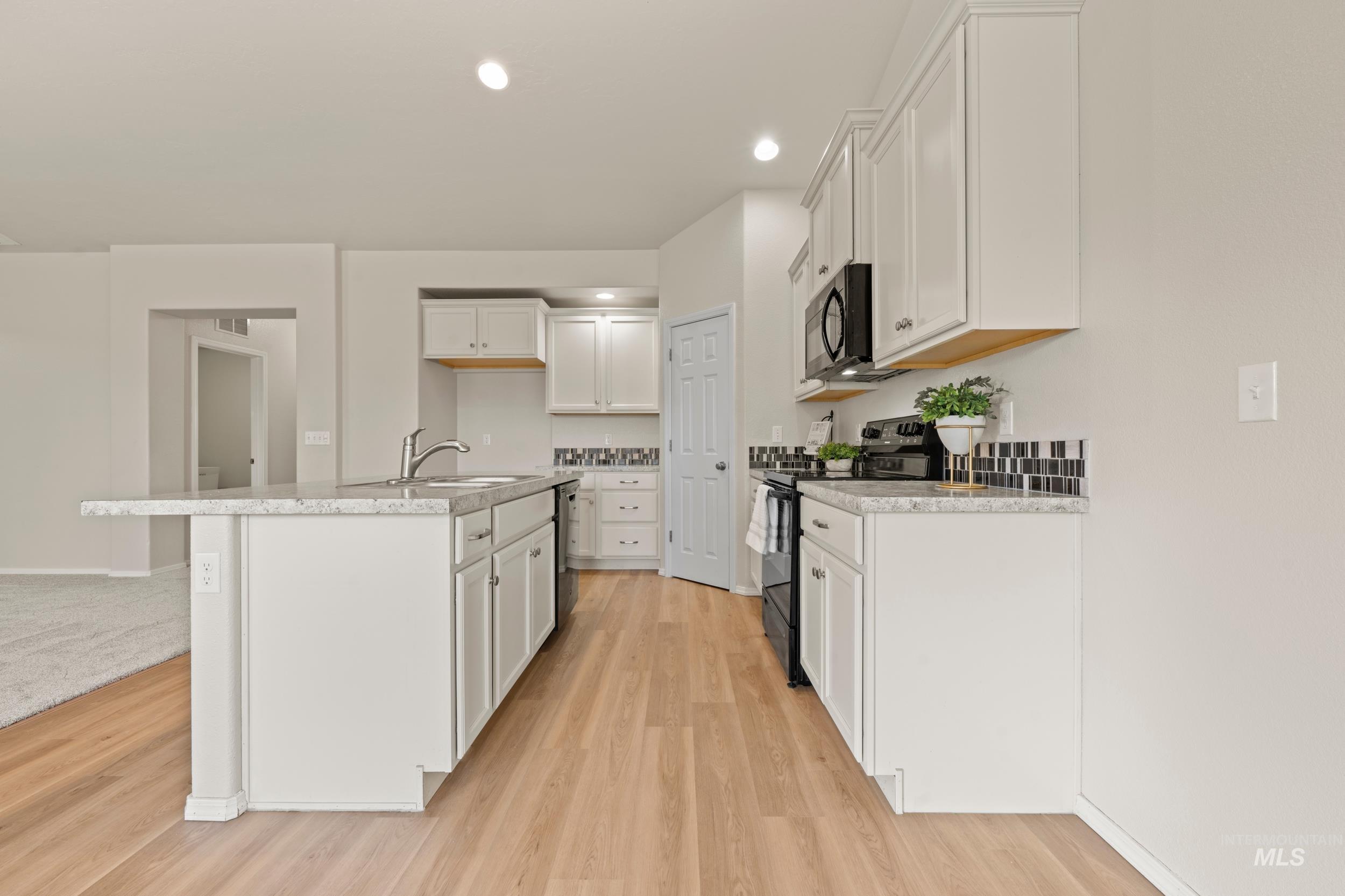 Kitchen with recessed lighting, black appliances, white cabinets, light wood finished floors, and a center island with sink